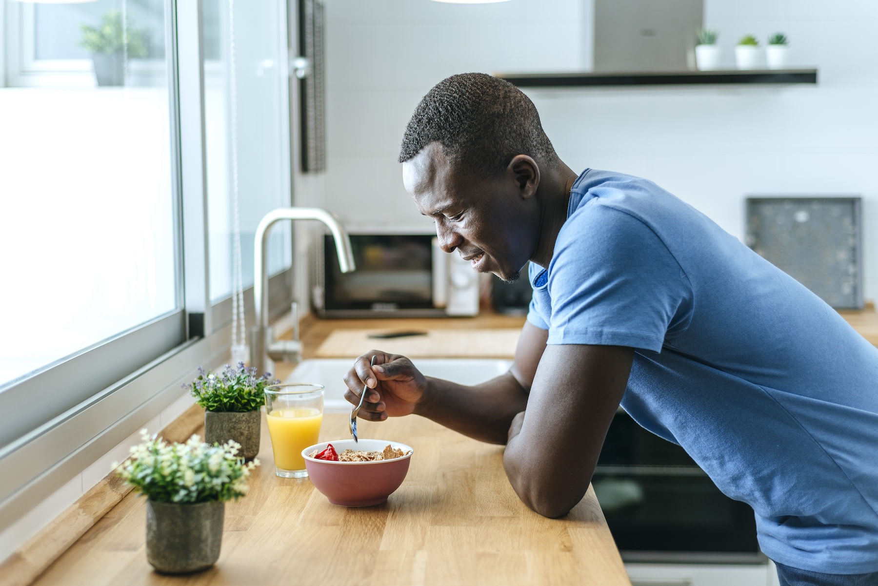 A happy man leaning on his kitchen counter while eating breakfast before a workout.