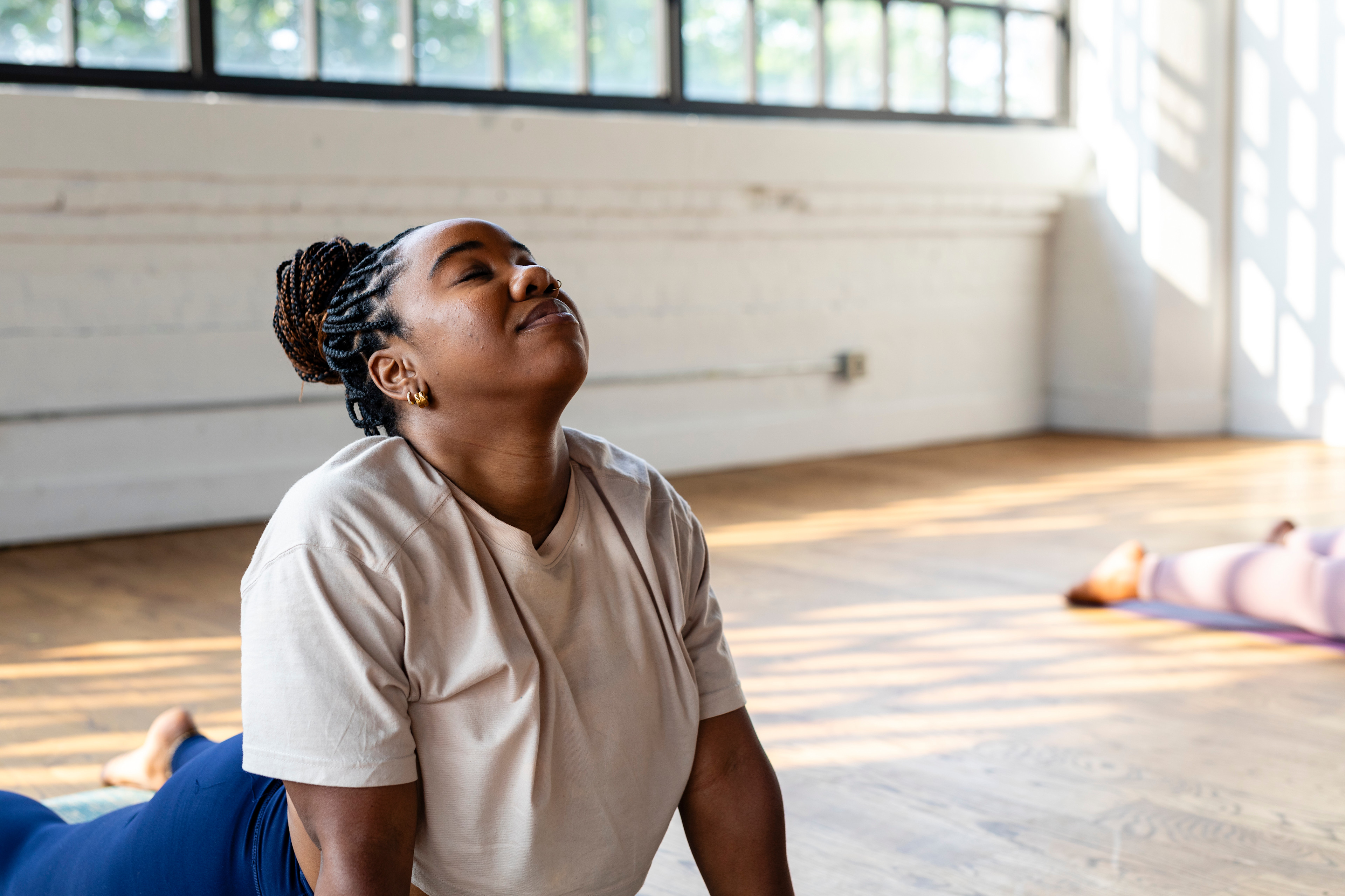 Woman doing easy yoga poses during a yoga class in a bright room on wood floors.