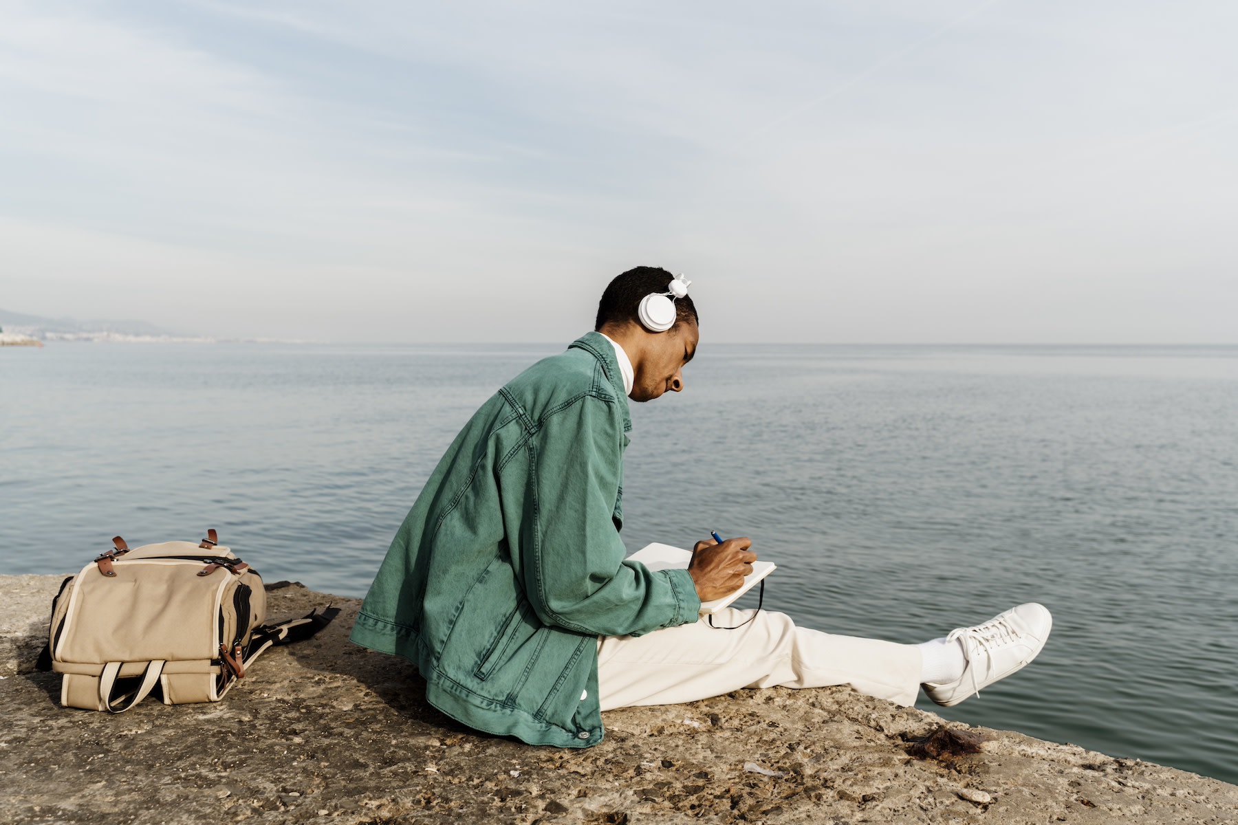 A man journaling while sitting on a rock by the sea.