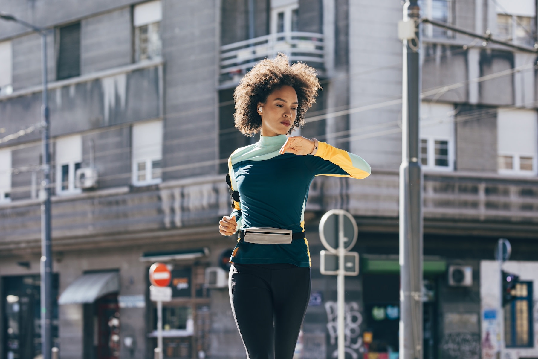 A runner checking her heart rate on a watch monitor while going for a run outside.