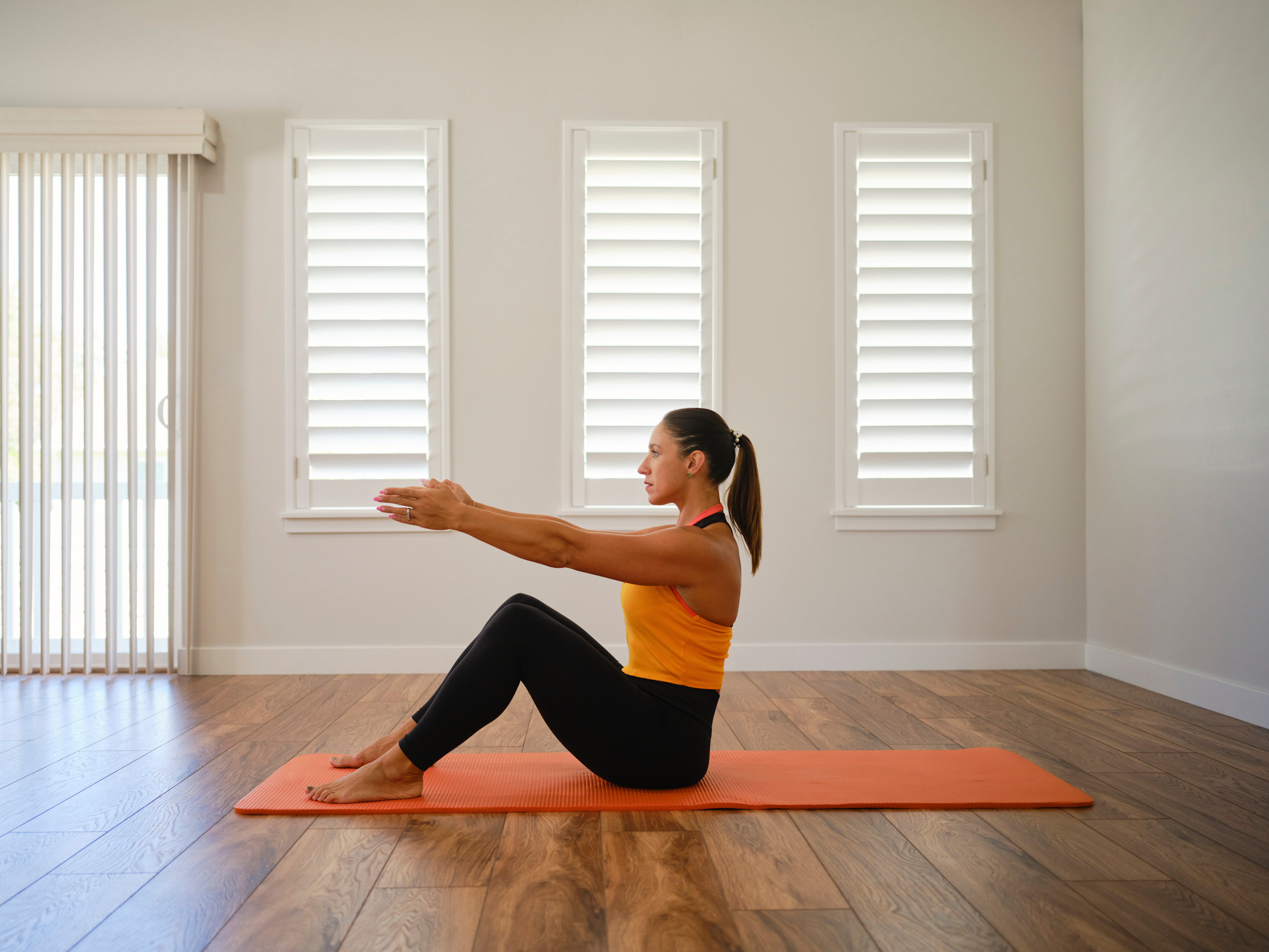 Woman doing a modified Pilates roll-up with bent knees in front of windows on an exercise mat