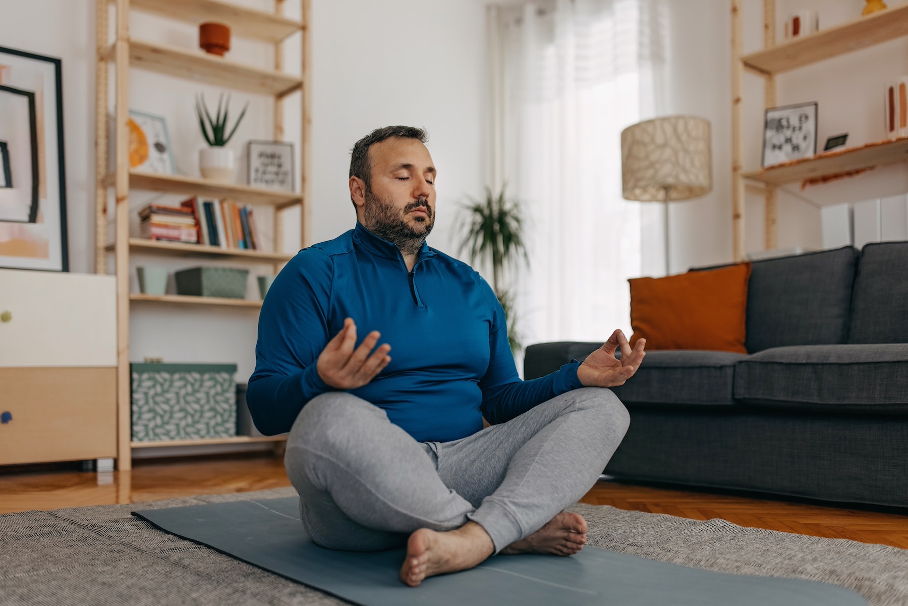 A man practicing daily meditation while sitting on the floor of his living room.