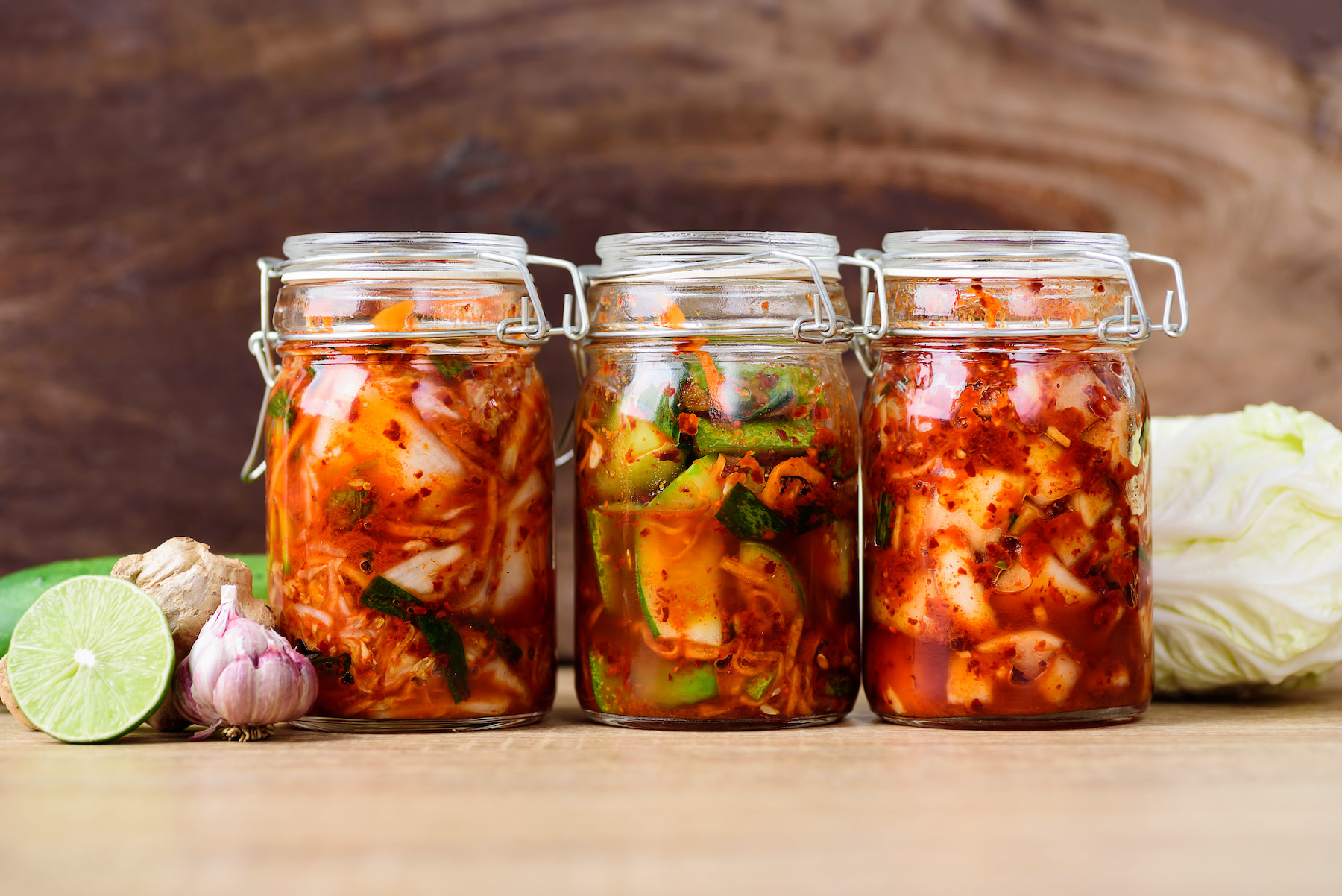 Three glass jars of kimchi sitting on a table. Fermented vegetables and other probiotic foods are great foods for gut health.