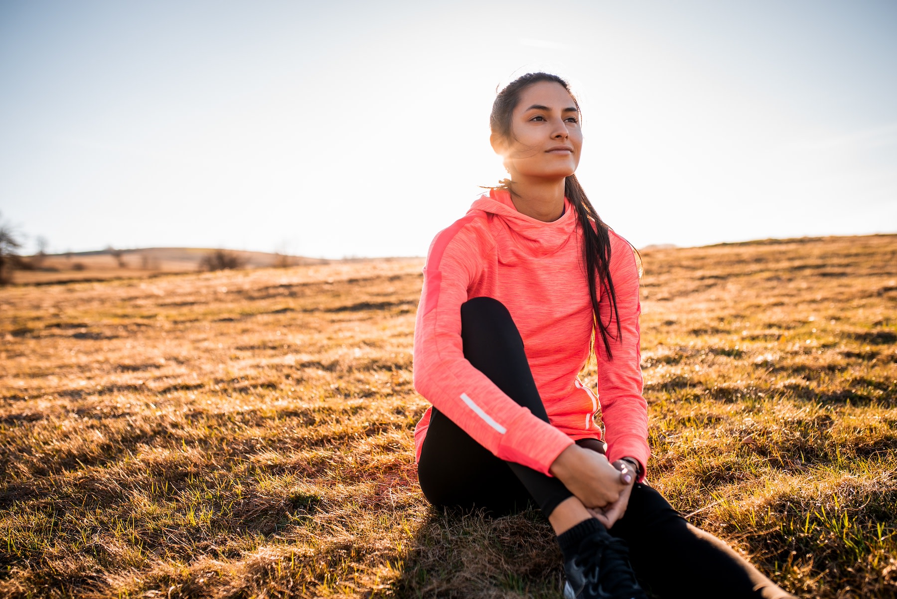 A calm, happy athlete sitting in a field at golden hour.