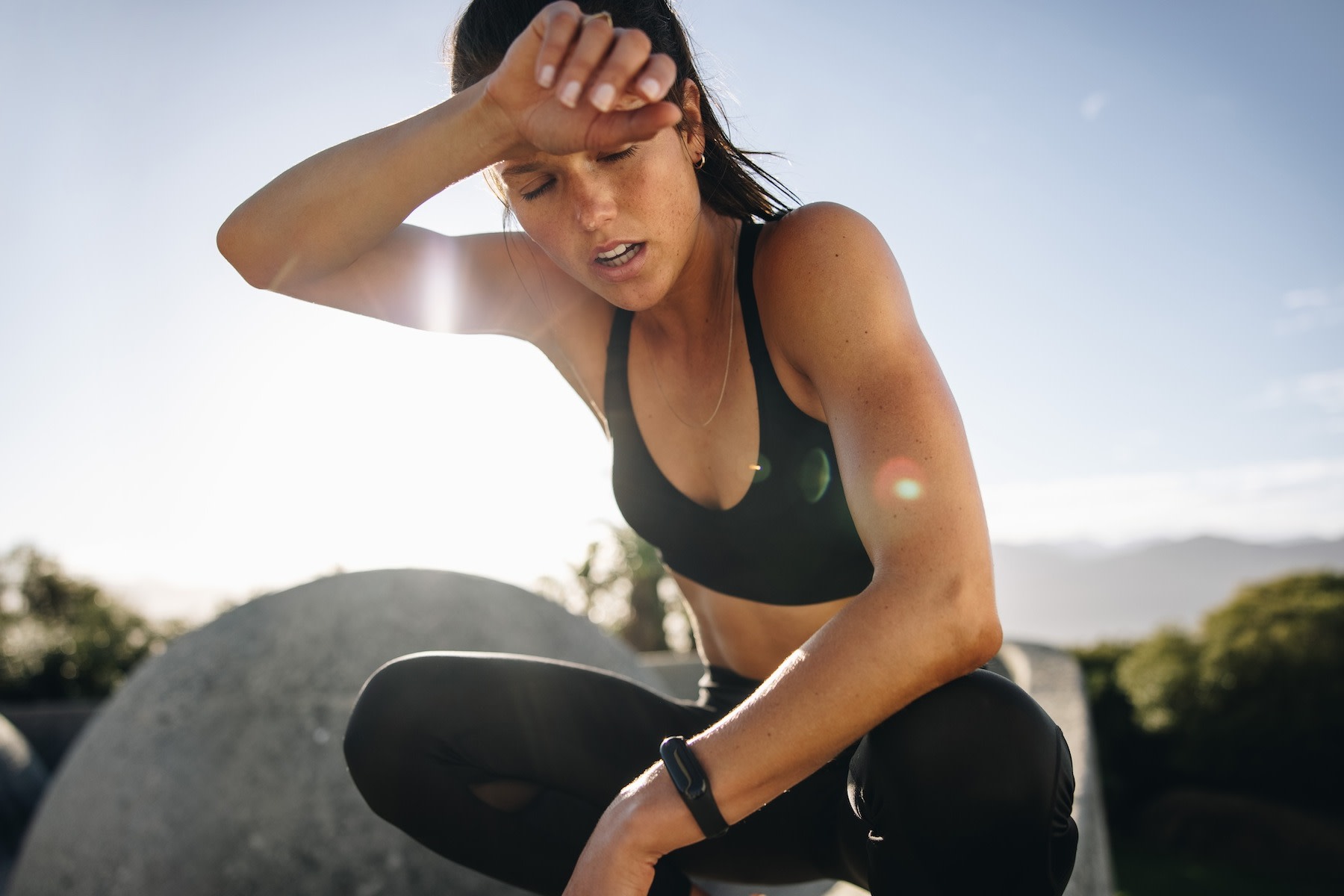 A woman experiencing bonking. She is kneeled down, exhausted, after a workout and wiping sweat off her face with her arm.