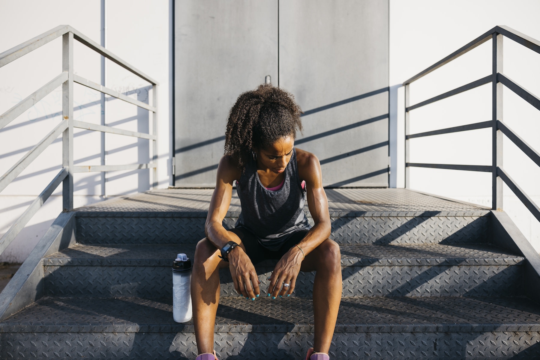 A tired athlete sitting outside on some steps. She's looking down and has her arms resting on her knees.