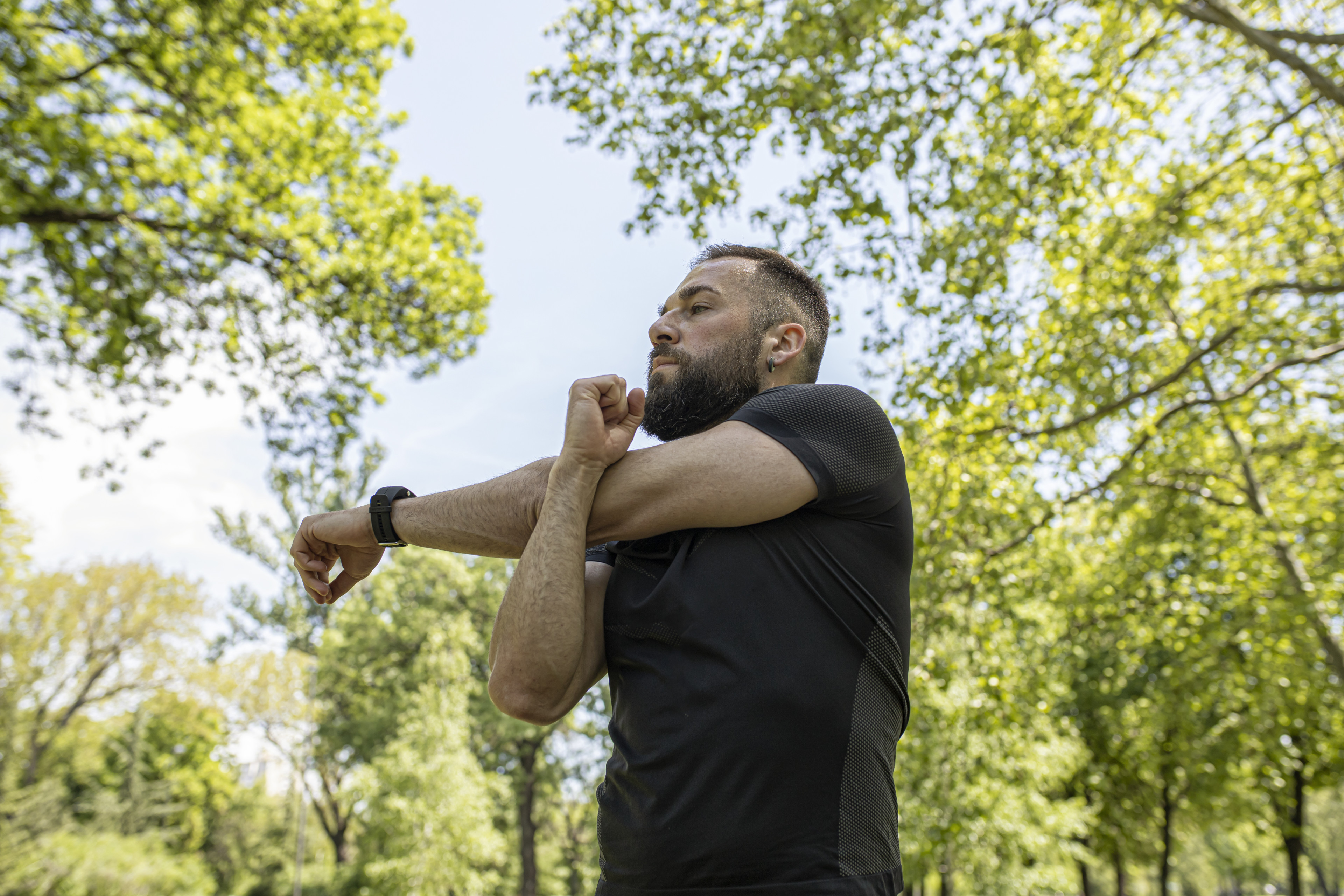 Man doing cross body shoulder stretch outside in park