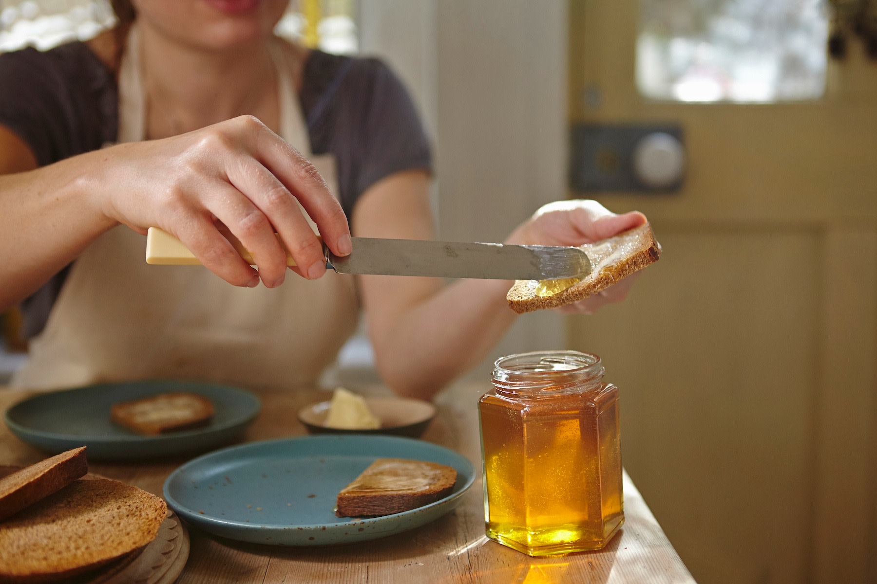 A woman spreading honey on a piece of bread to eat before a workout.