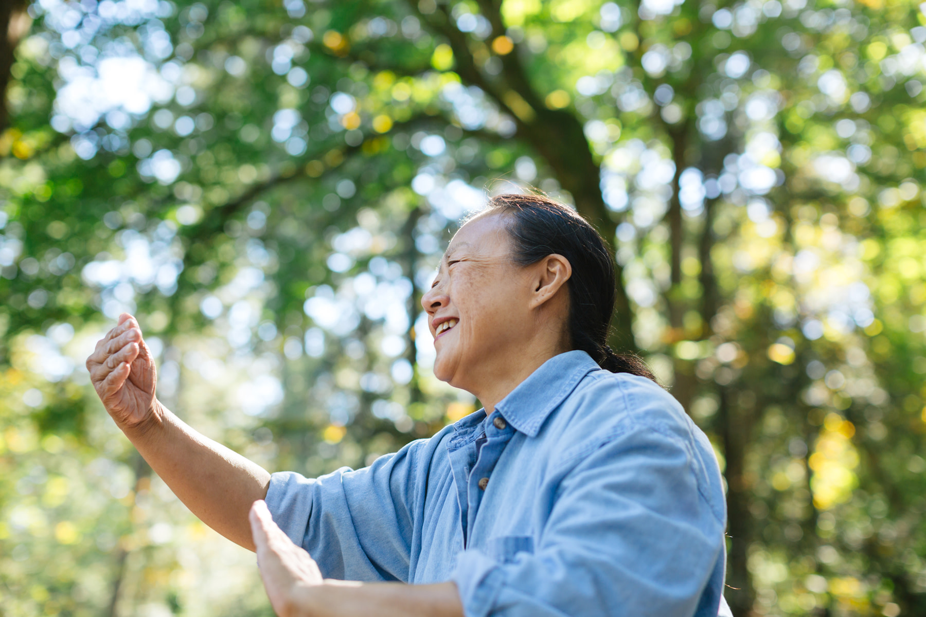 A woman smiling and practicing tai chi outside. Tai chi is a form of mindful movement.