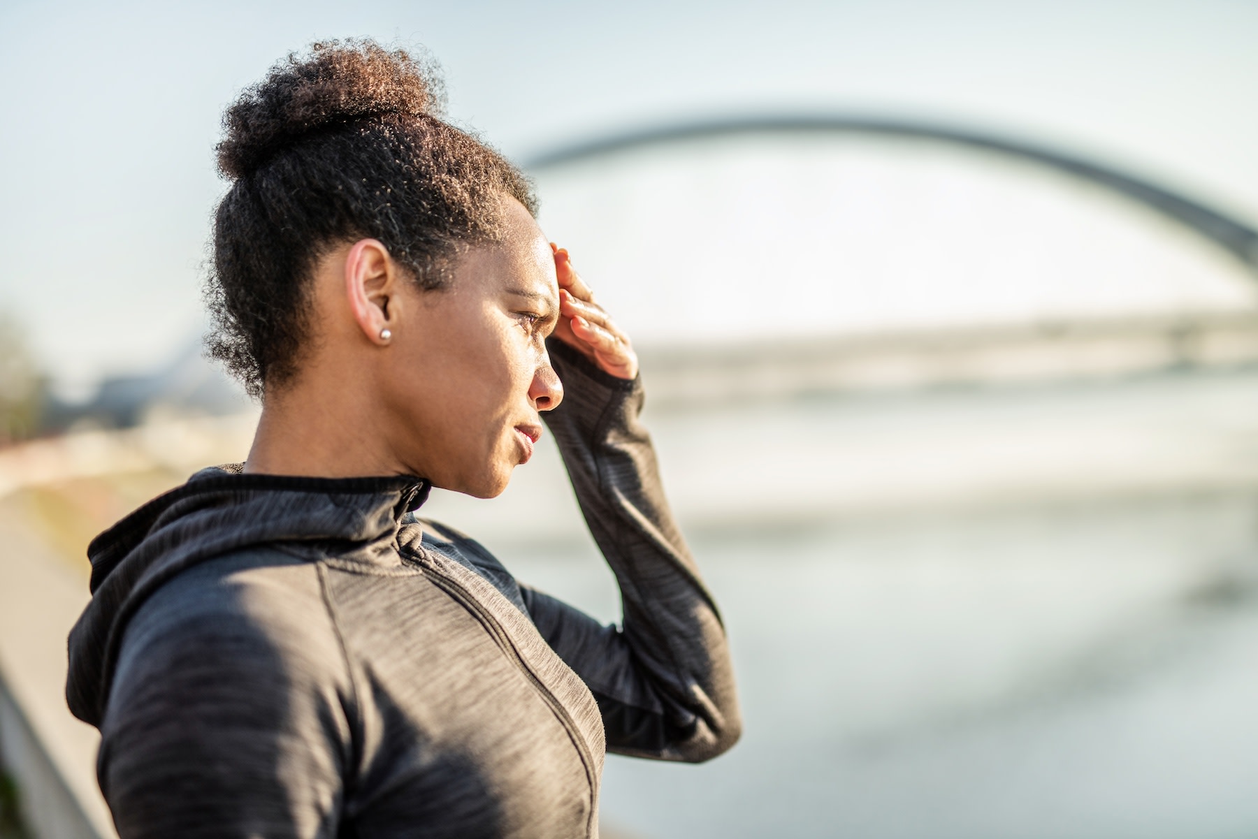 A woman standing outside and holding her hand to her face as she suffers from a headache after a workout.