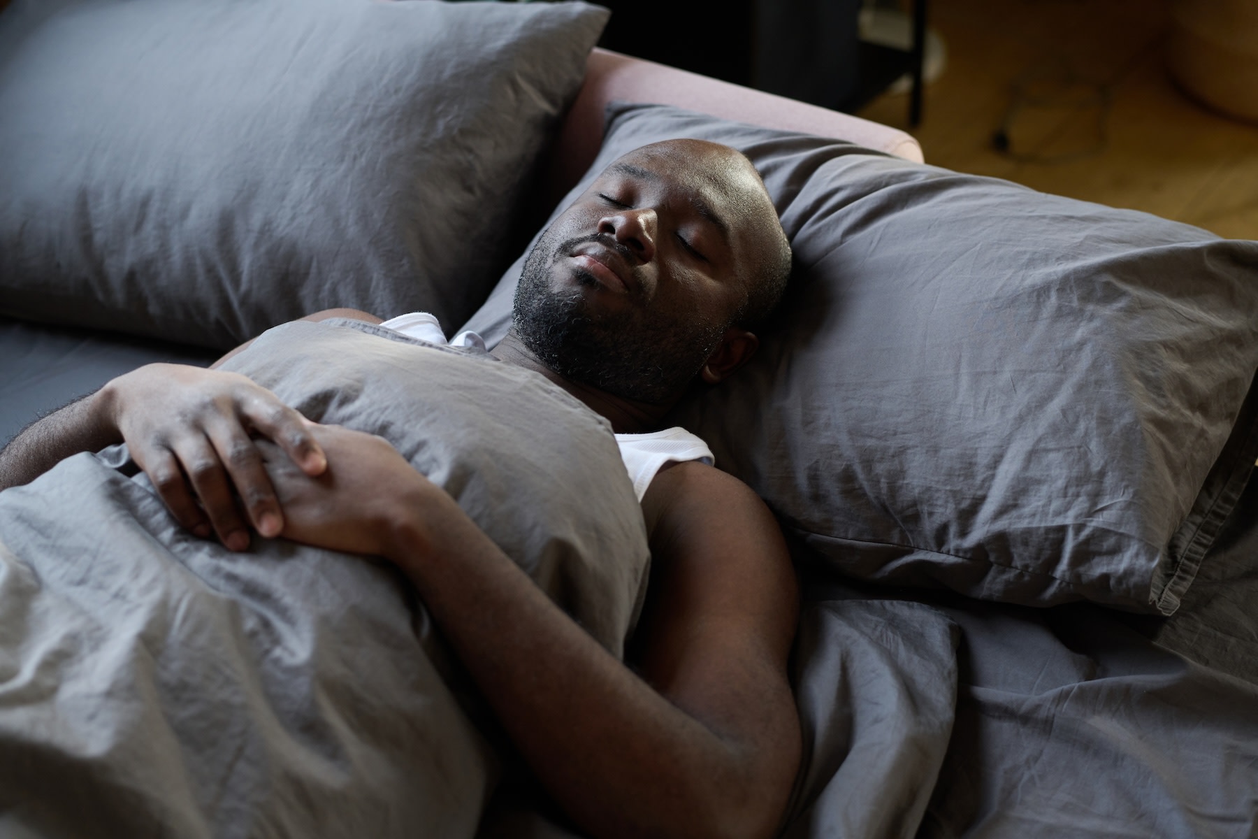 A man closing his eyes and relaxing peacefully in bed while practicing progressive muscle relaxation.