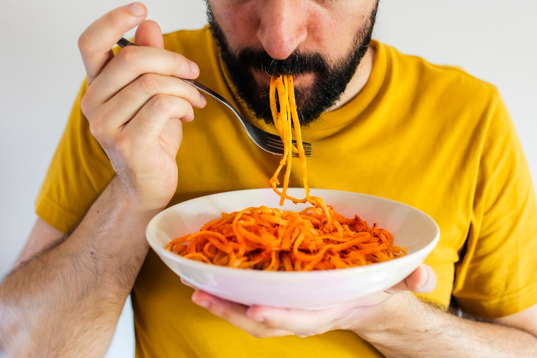 A close-up photo of a man eating a bowl of spaghetti as he eats before a marathon.