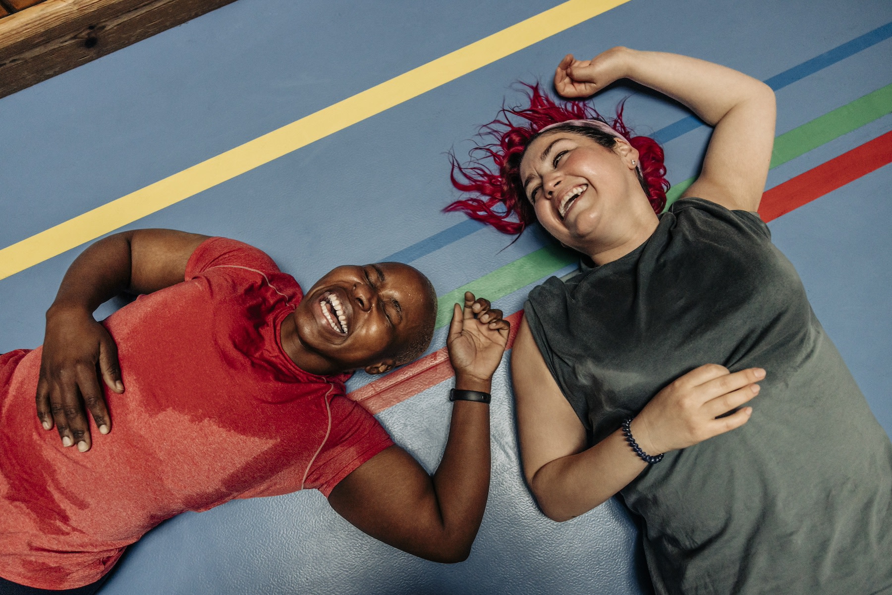 Two women lying down on a colorful exercise mat after exercising, laughing. Exercising is a great way to activate your "happy hormones."