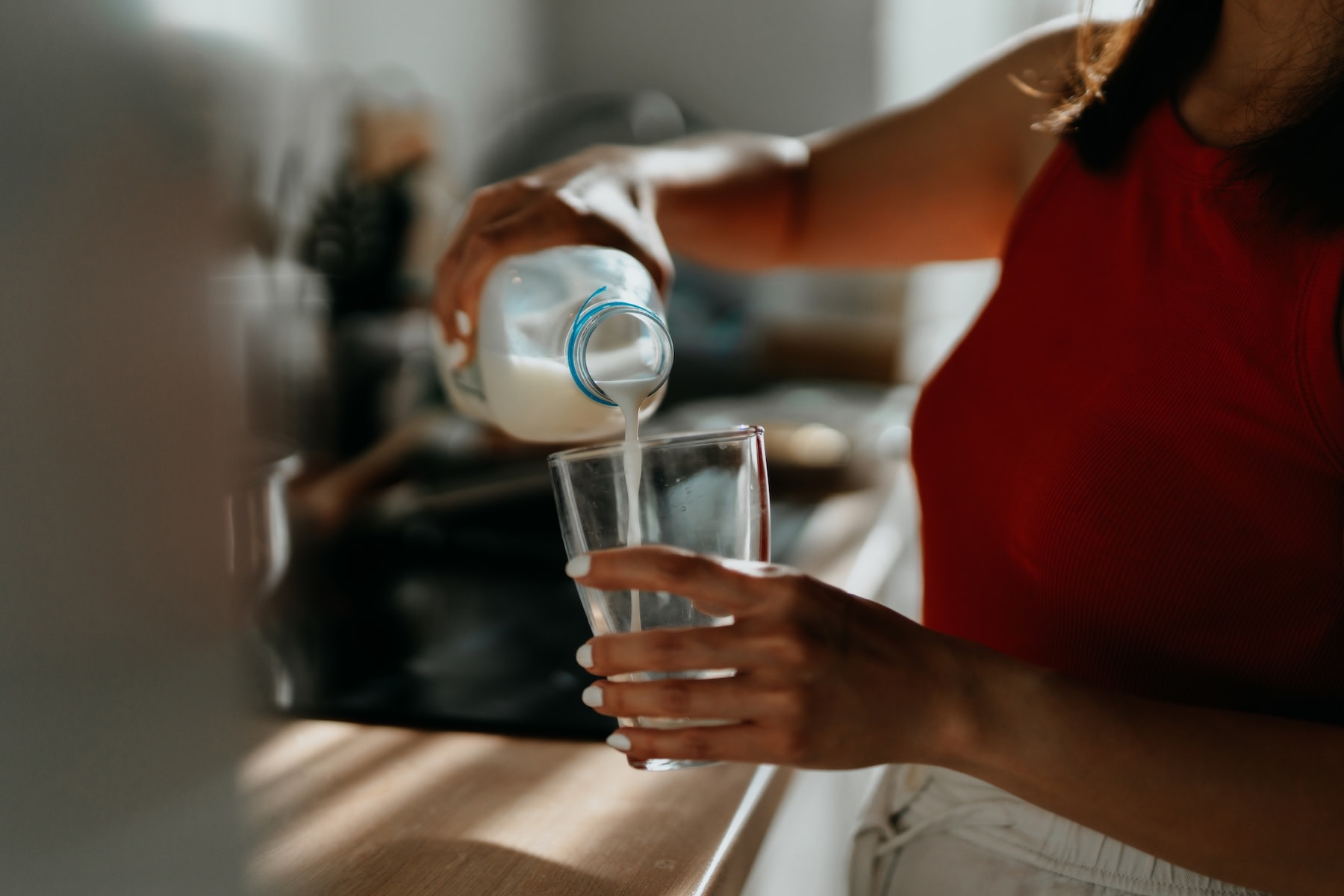 Close-up photo of a woman pouring a glass of milk in her kitchen. She's drinking milk to help build muscle. 
