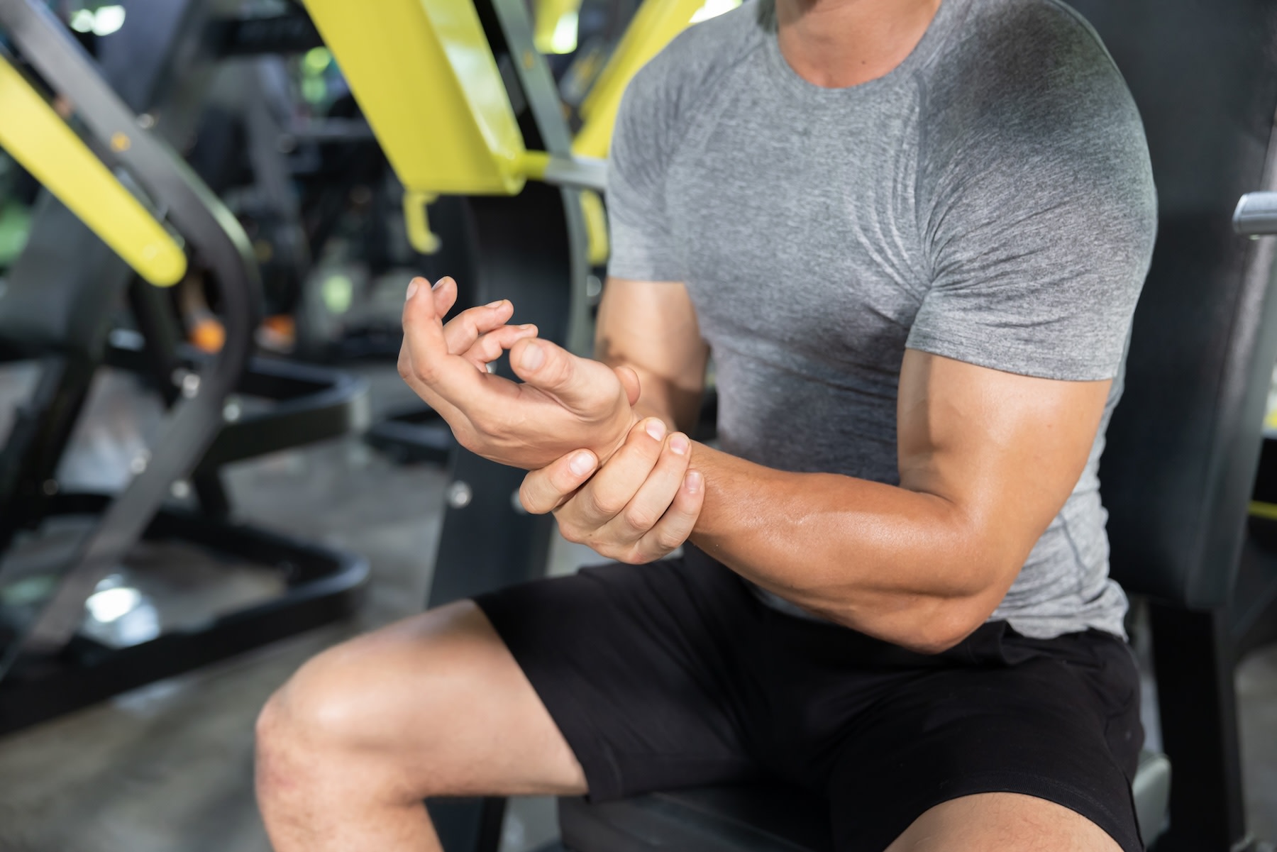Close-up photo of a man holding his left wrist in the gym. He is dealing with wrist pain from weight lifting.