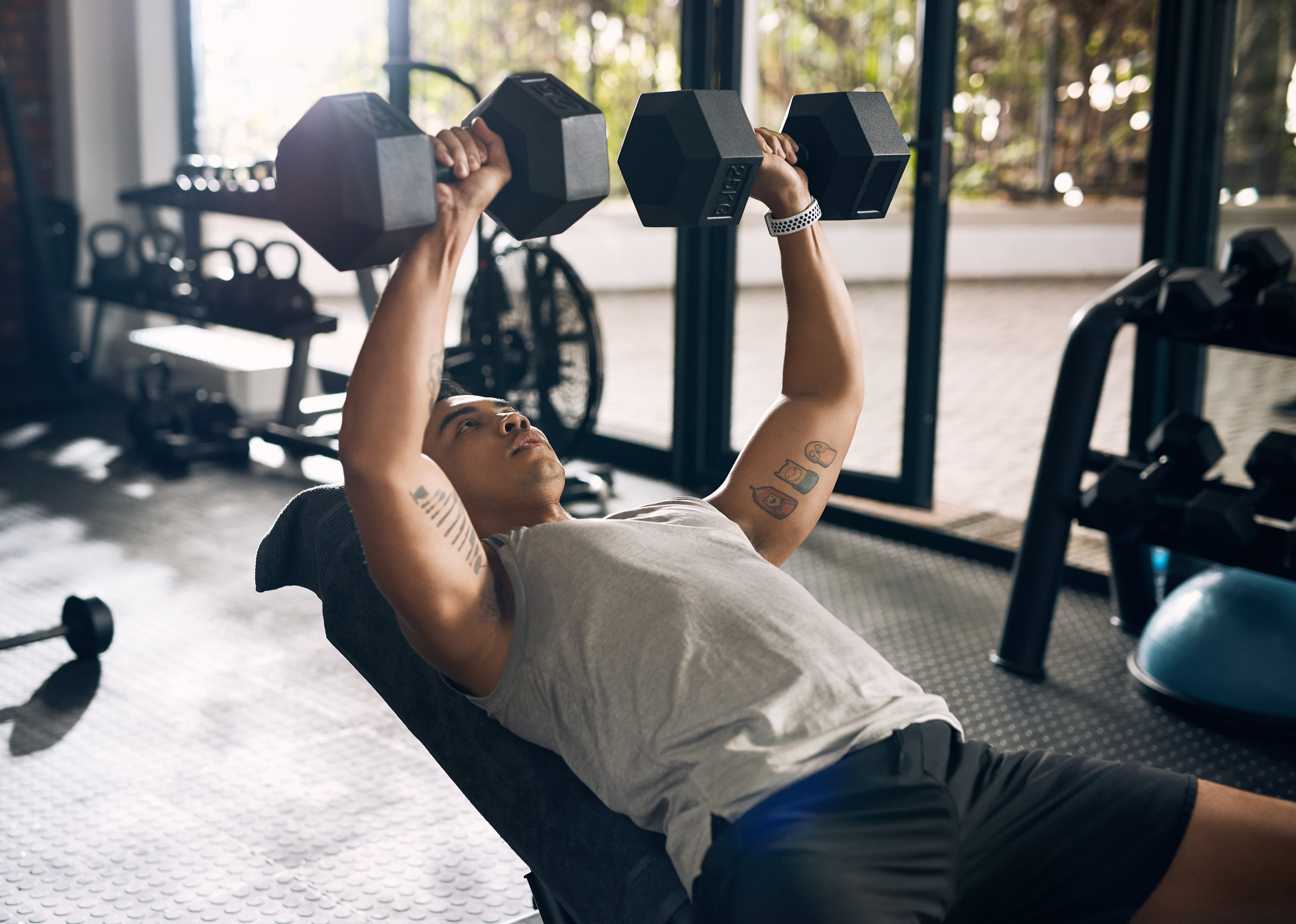 A young man does incline dumbbell chest presses at the gym to build chest muscles