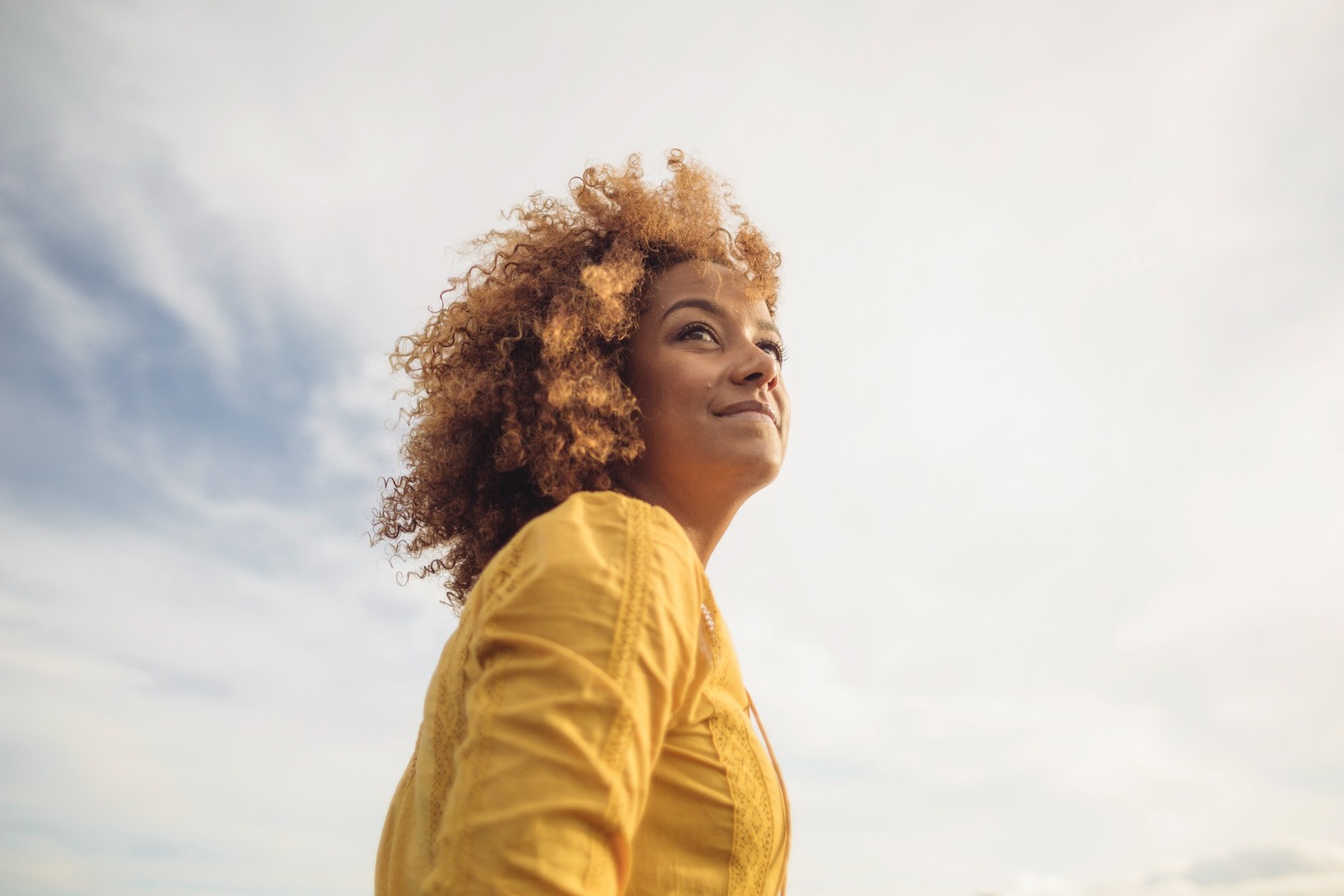 A low-angle portrait of a woman looking up at the sunny sky.