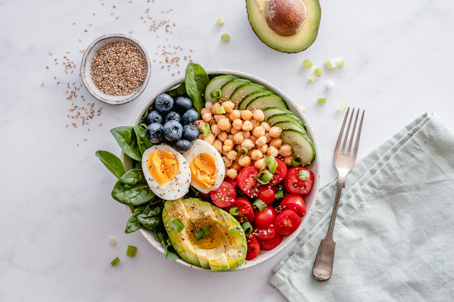 A wholesome bowl filled with macronutrient sources, including avocado, hard-boiled egg, chickpeas, spinach, tomato, blueberries, and cucumbers.