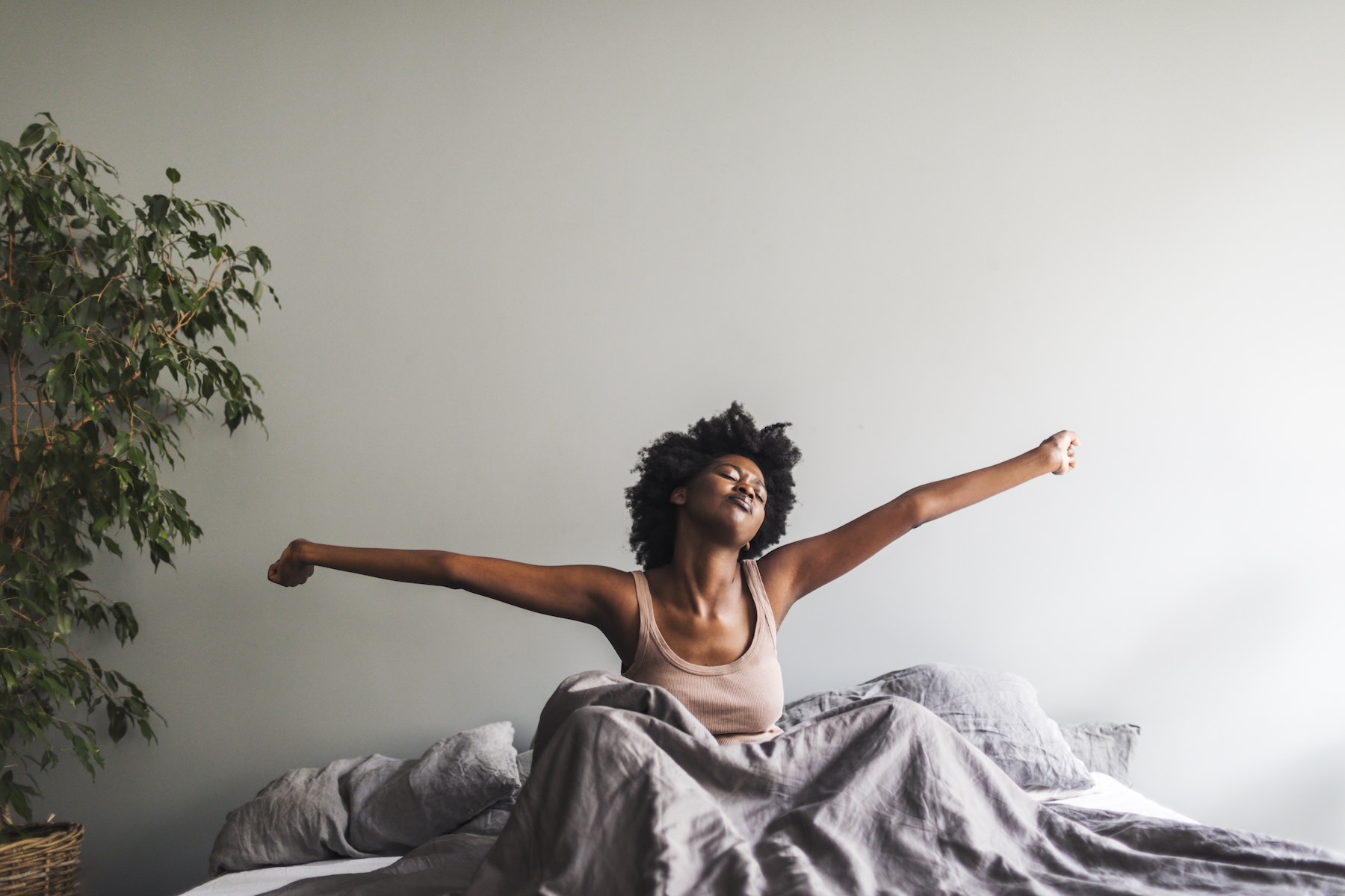 A woman sitting up and stretching her arms out to her side in bed after waking up.