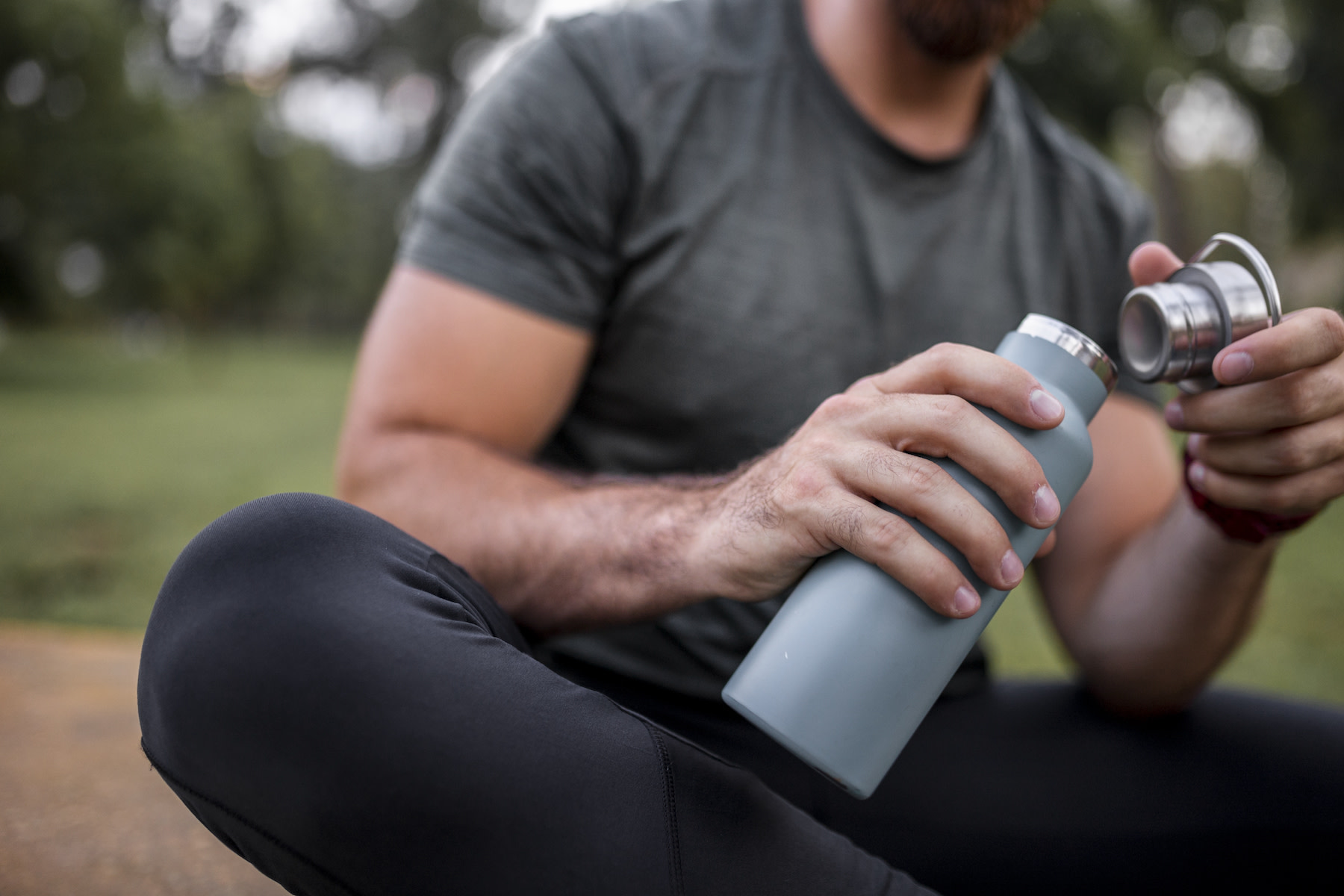 A close-up photo of a person closing a reusable water bottle while sitting down outside.