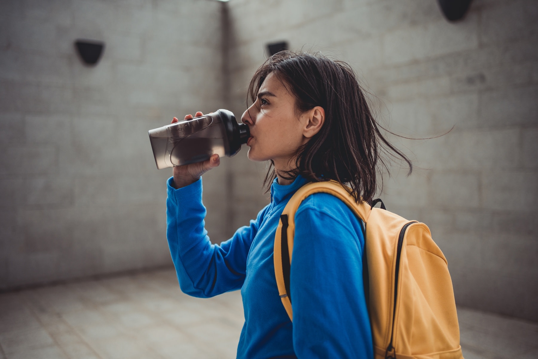 A woman having creatine while sipping from a black shaker bottle after an outdoor workout.