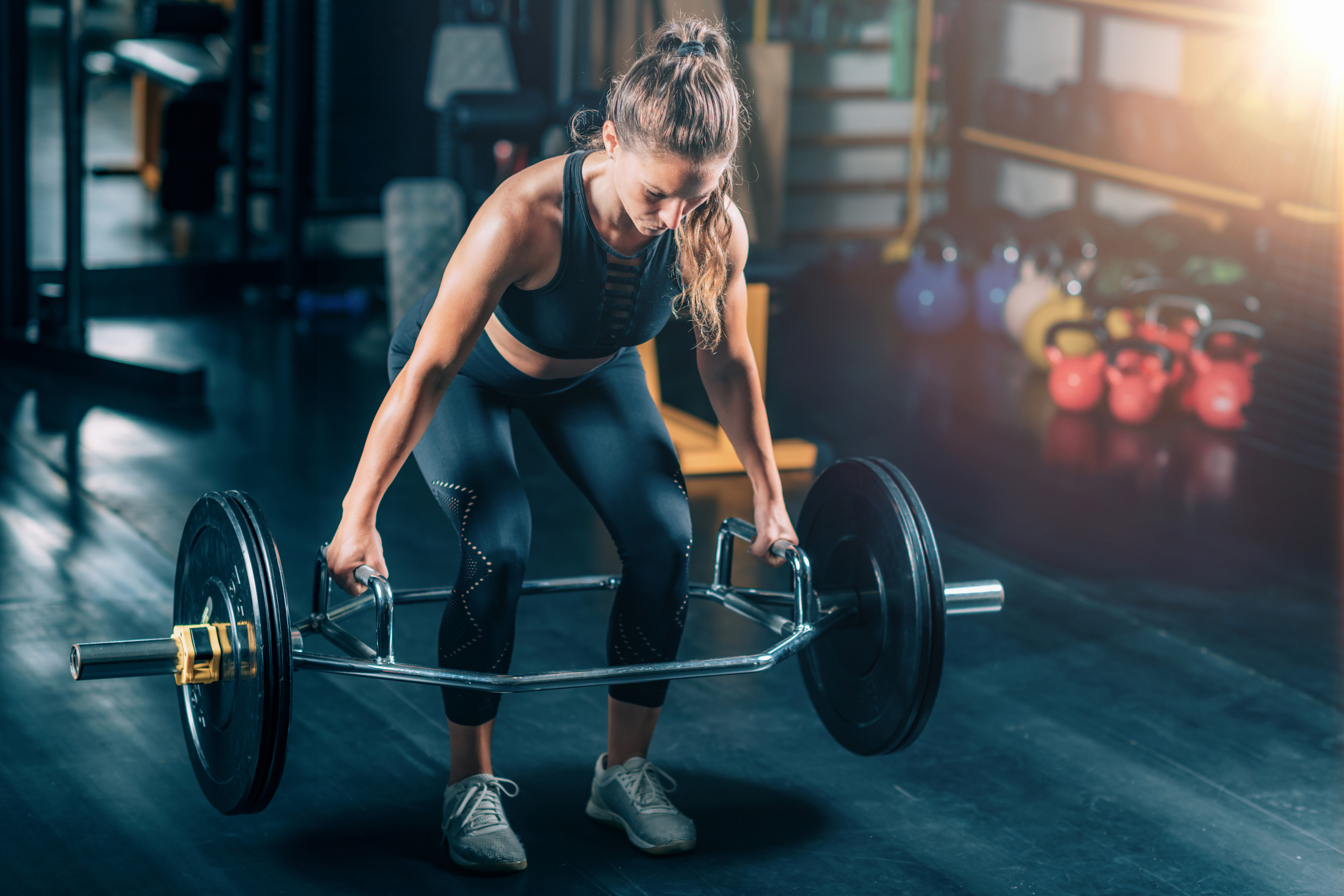 Woman doing a barbell deadlift with a loaded trap or hex bar in the gym