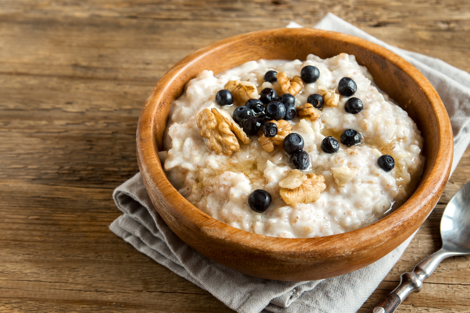 A wooden bowl of oatmeal, walnuts, and blueberries, which is a great bedtime snack to help you sleep.