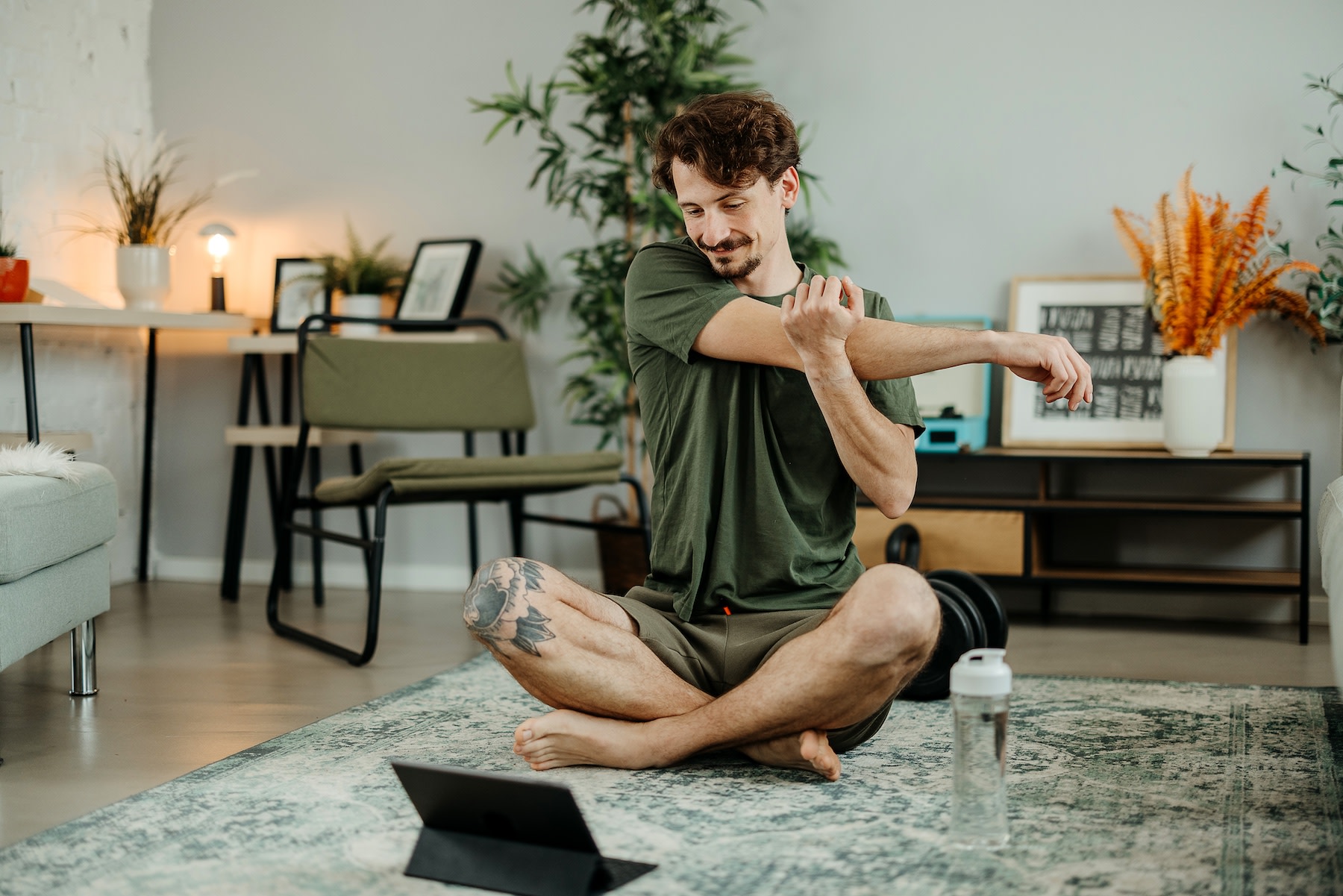 A man stretching his arms while doing a guided stretching class on his tablet after a workout.