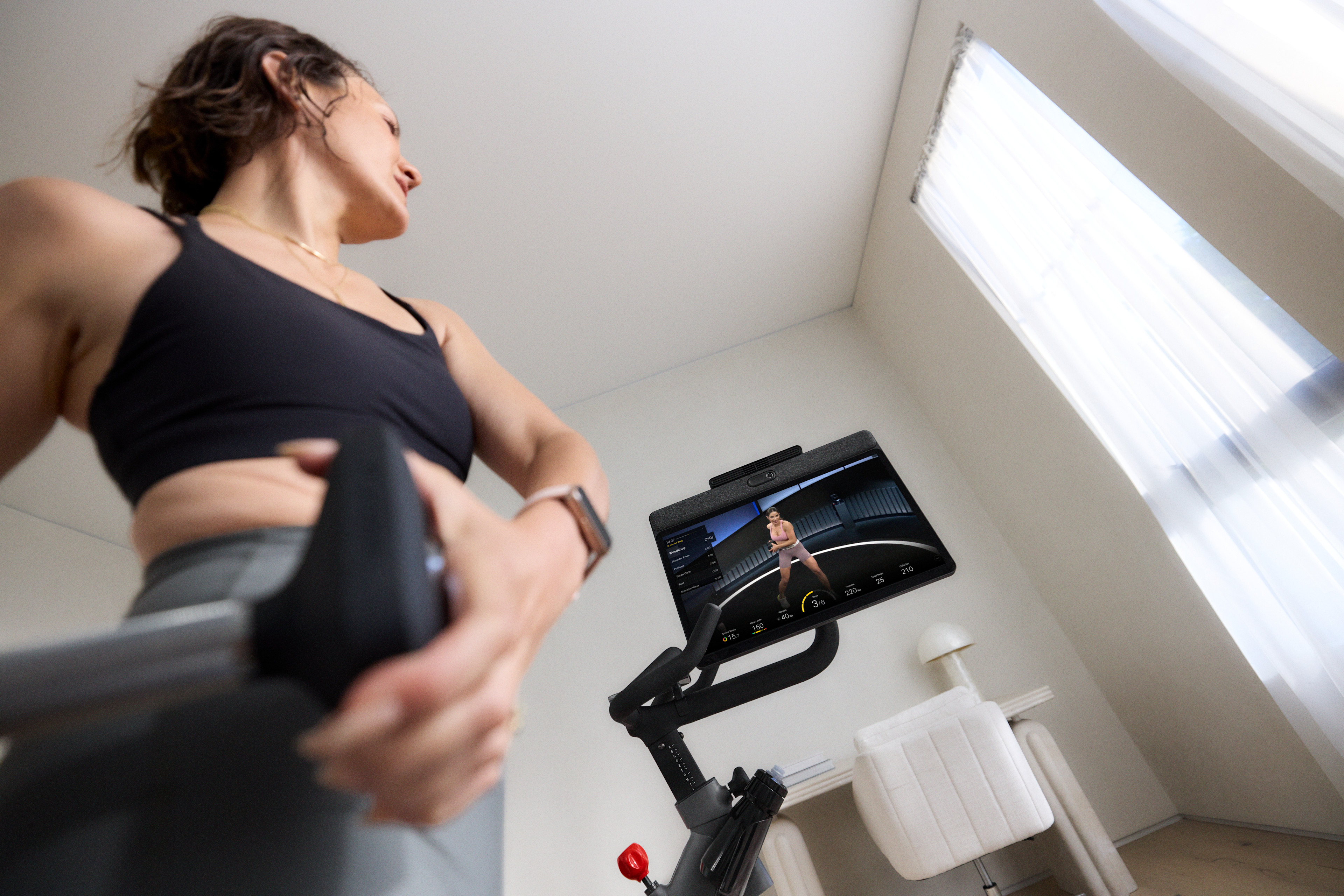 Woman lifts weights during a cross training workout for cycling while standing next to a Peloton Bike+.