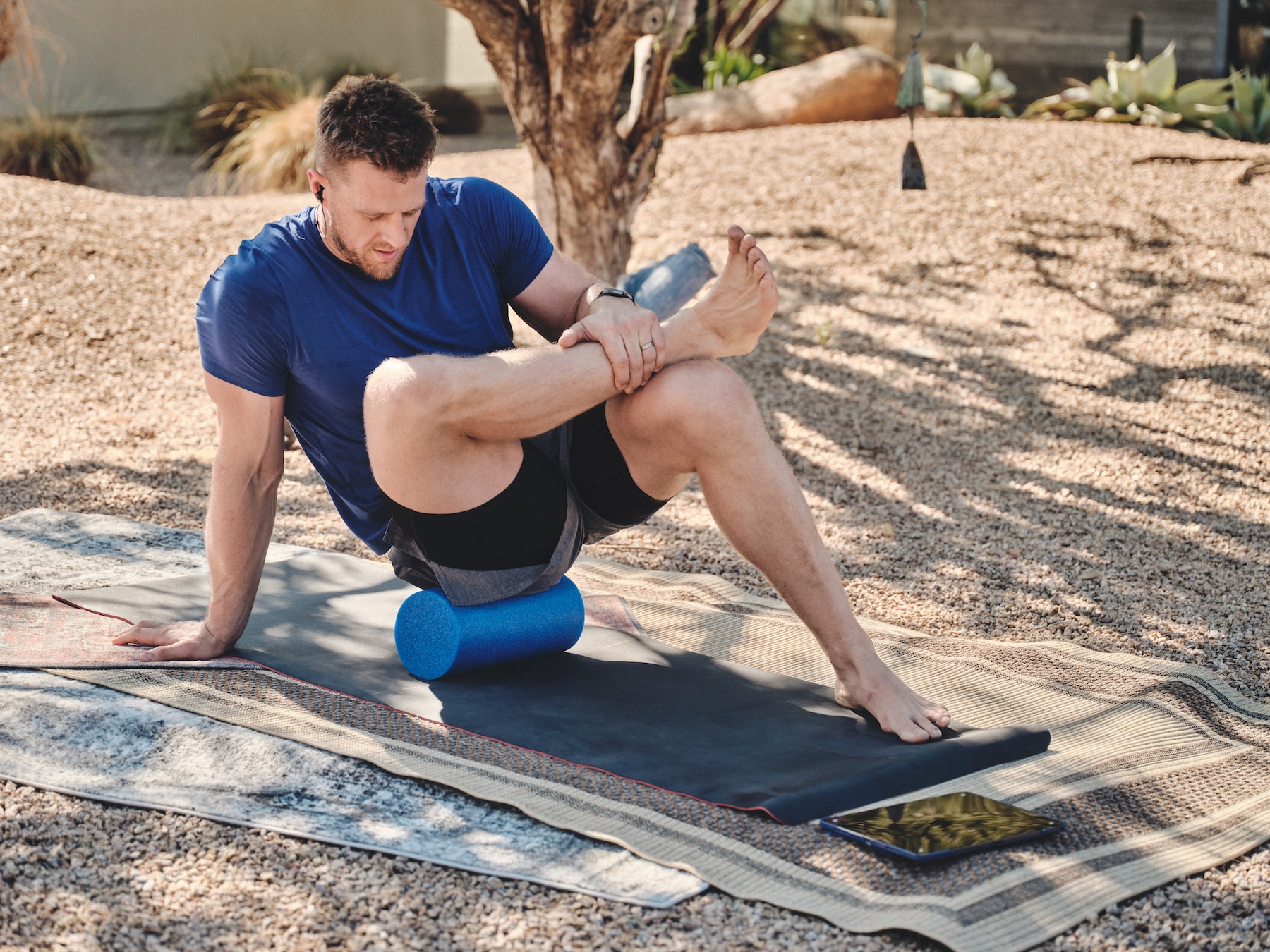 JJ Watt foam rolling on a yoga mat outside using a Peloton class to guide him through it.