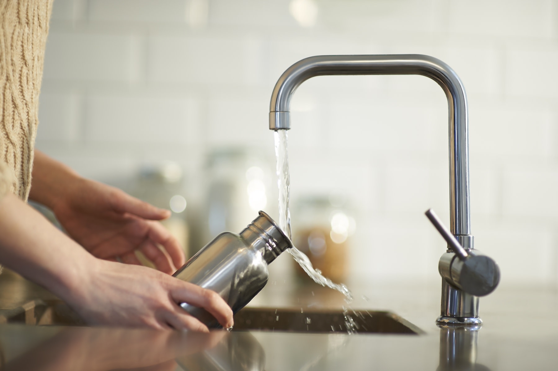 A person cleaning a stainless steel water bottle in the sink as they rinse it with water.