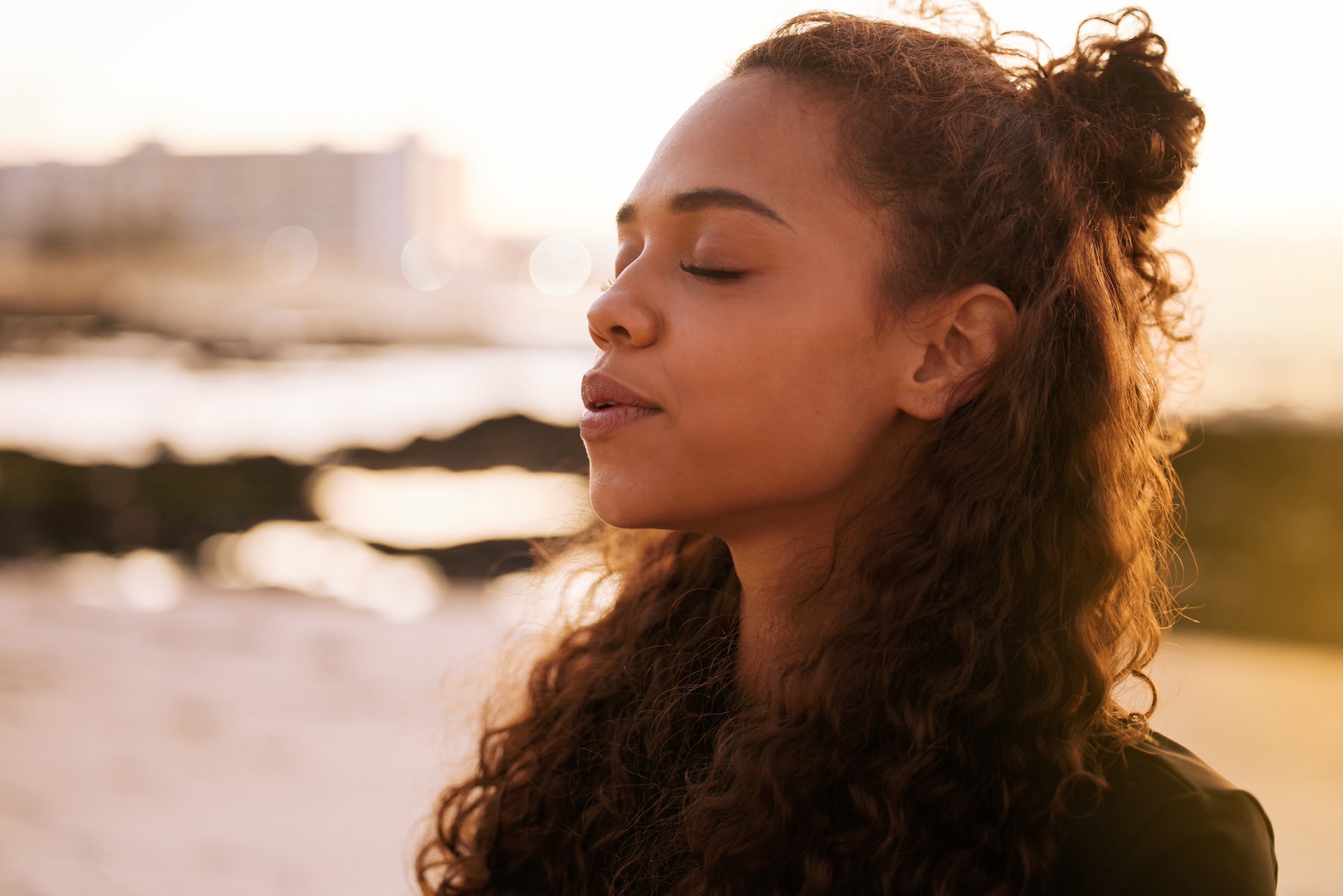 A young woman practicing the box breathing technique outdoors. Her eyes are shut and her face looks calm.