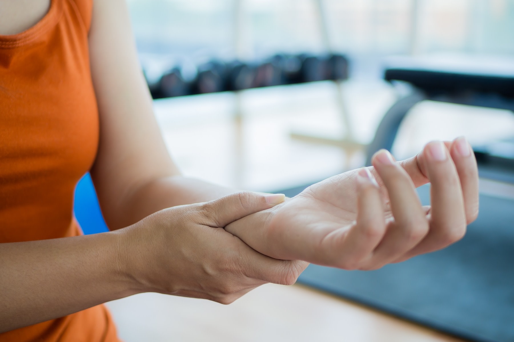 Close-up photo of a woman holding her left wrist in the gym. She is dealing with wrist pain from weight lifting.