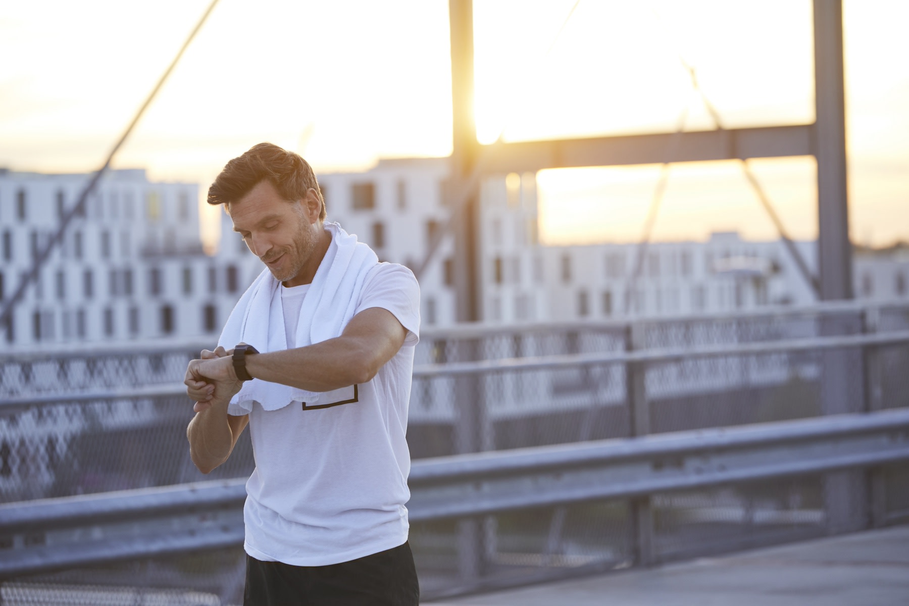 A man checking his heart rate using a heart rate watch as he cools down from an outdoor run at dusk.