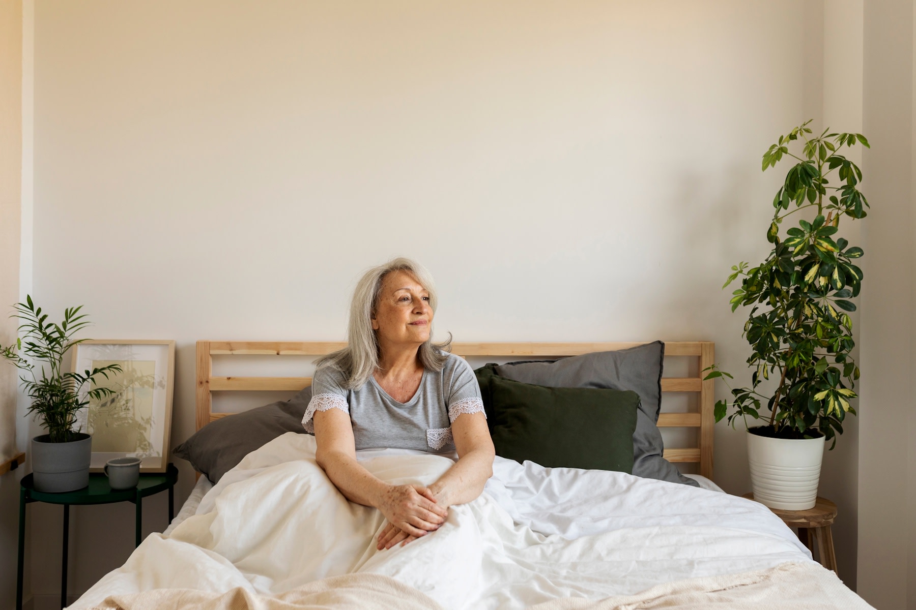 A calm woman sitting in bed practicing mindfulness and looking to her left as she focuses on how to be more present in her daily life.