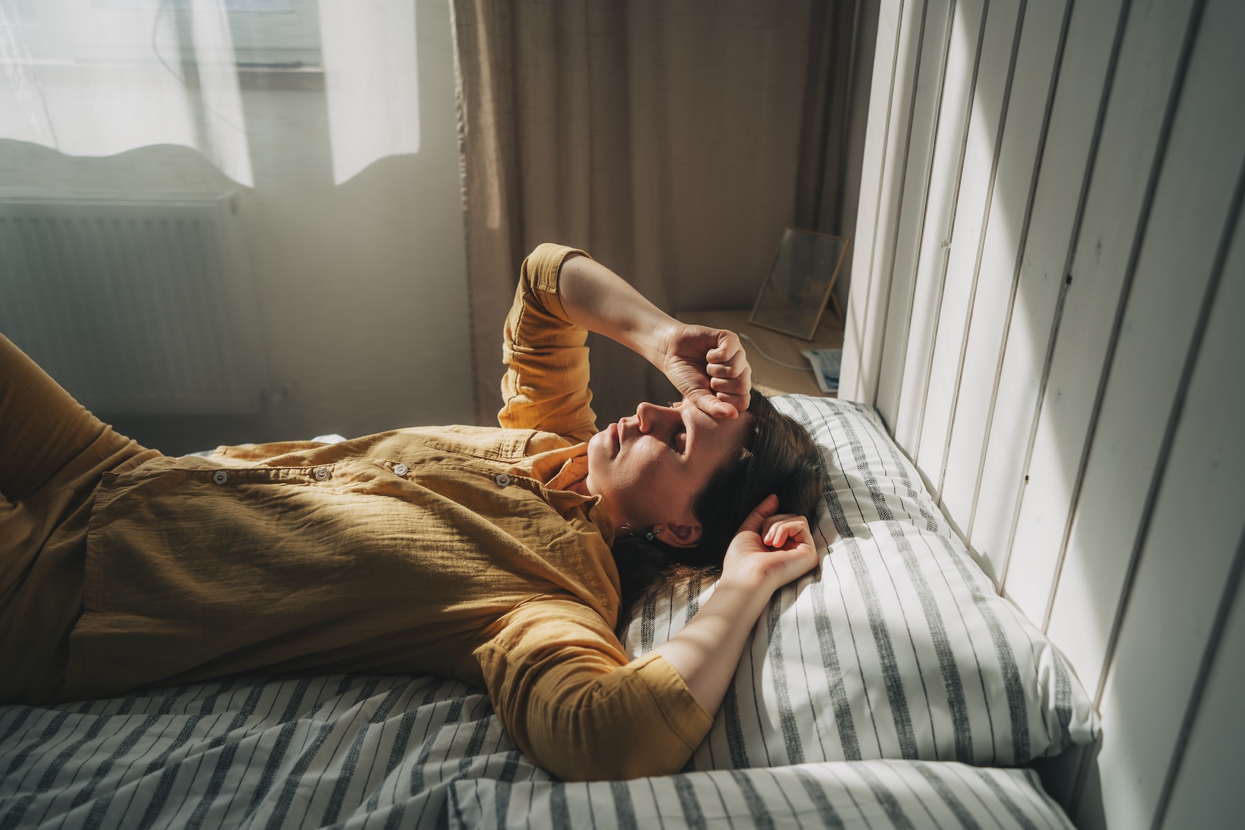 An overtired woman looking stressed out while lying in her bed in the early morning.