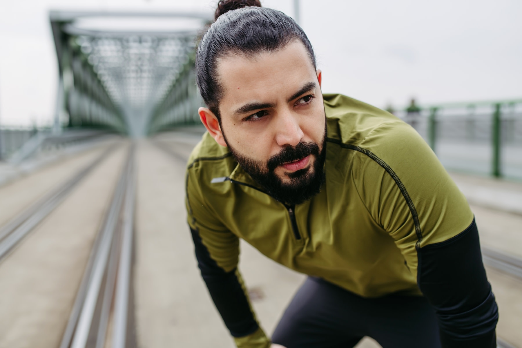 A man exhaling as he puts his hands on his knees while standing up outside. He's dealing with a stomach ache after exercise.