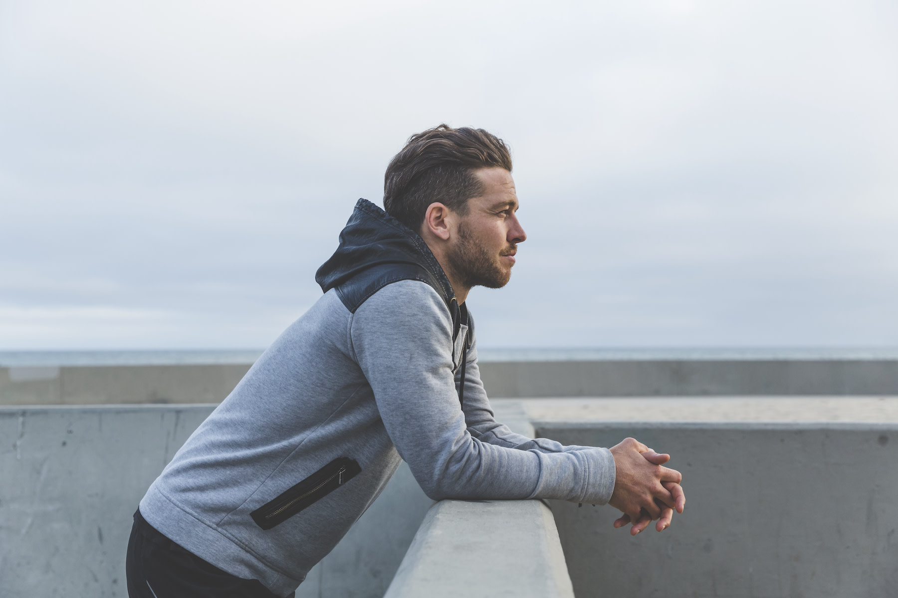 How to Change Your Mindset: A young man leaning his arms on a ledge while looking out thoughtfully at the sea.