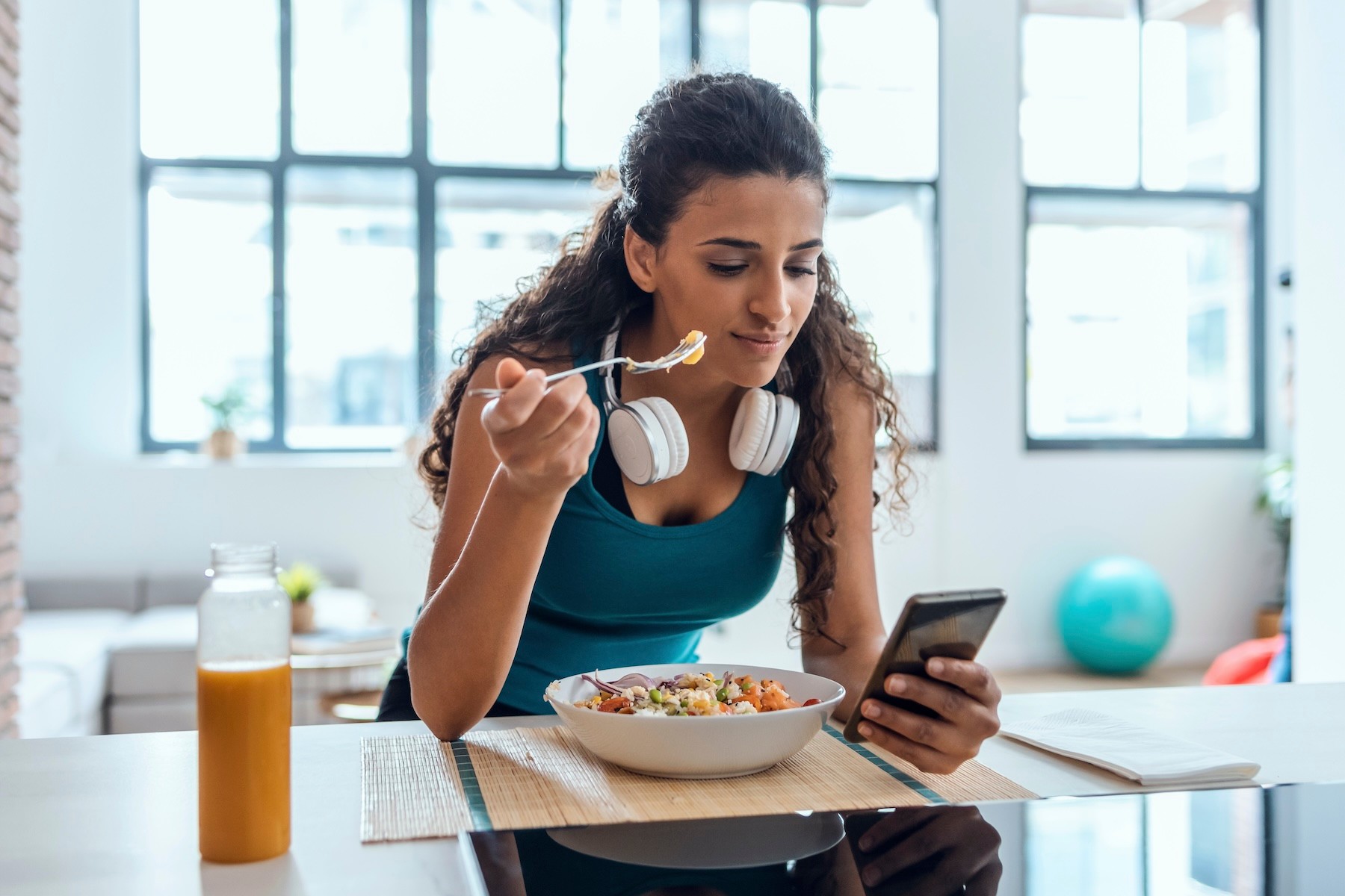 A woman eating after a workout and looking at her phone.