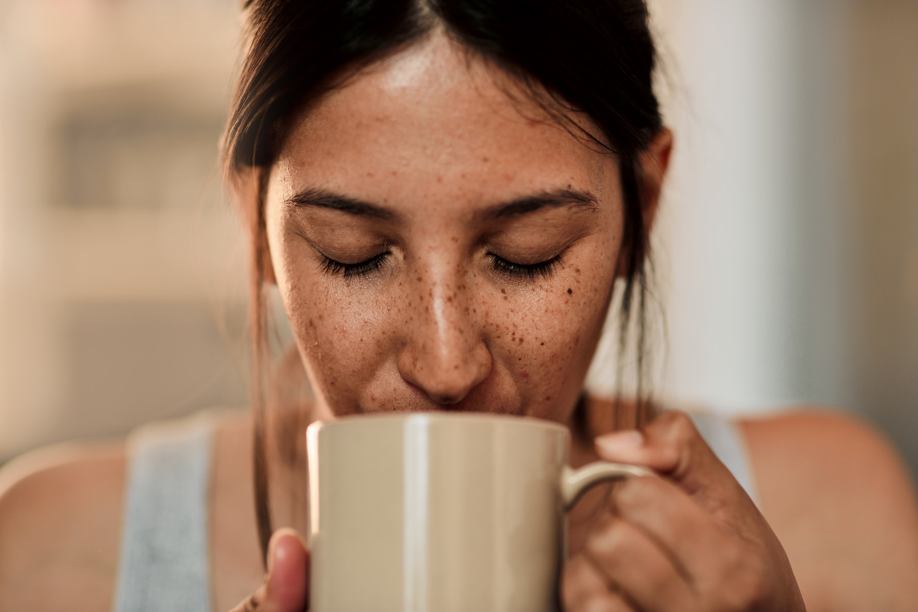 Does Coffee Dehydrate You?: Close-up photo of a woman with freckles drinking a cup of coffee from a mug.