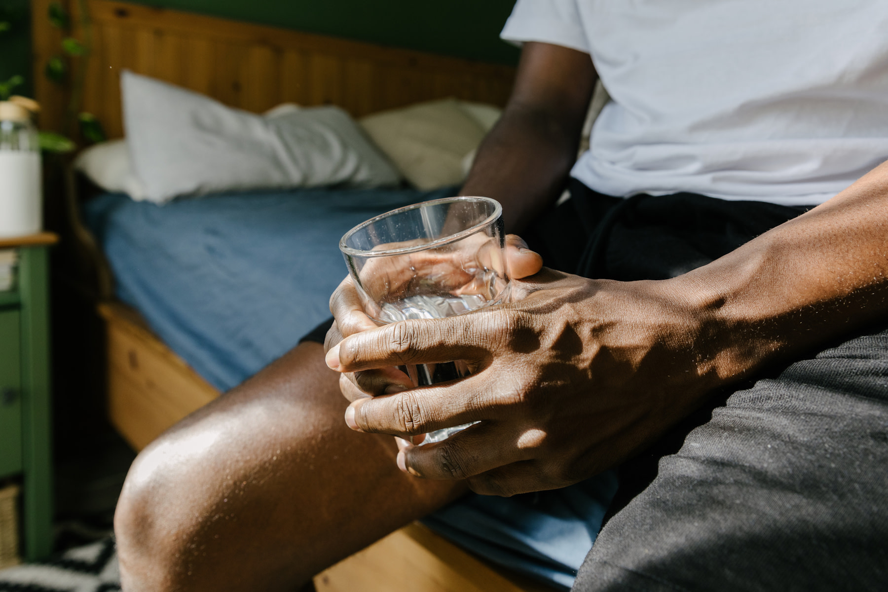 A man holding a glass of water as he drinks water before bed.