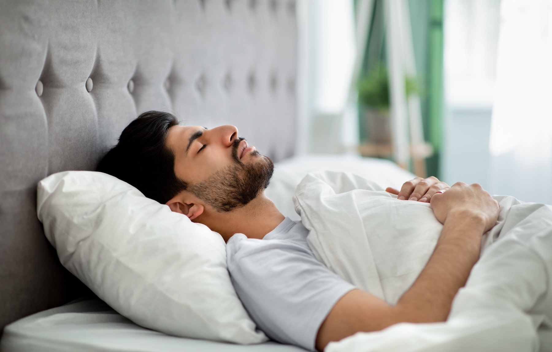 A man lying down on his back in bed practicing a body scan meditation.