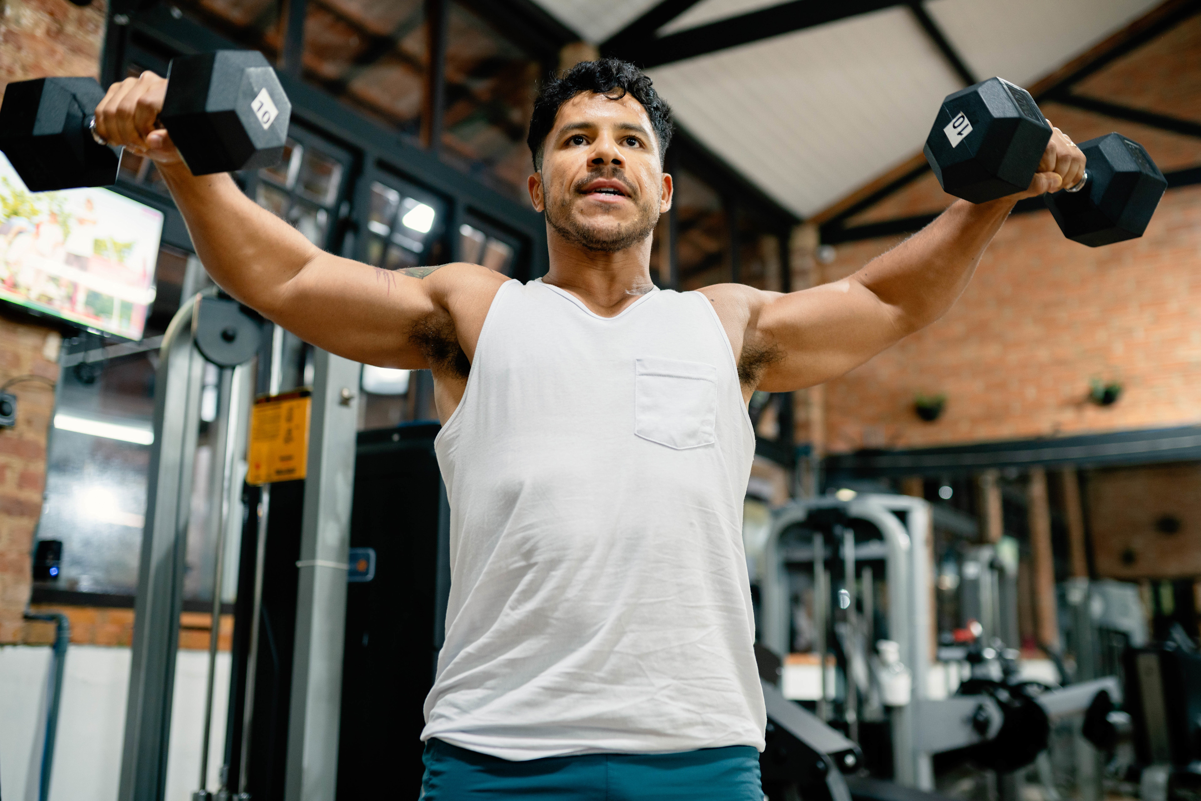 Man doing a lateral raise with dumbbells during a superset workout at the gym.