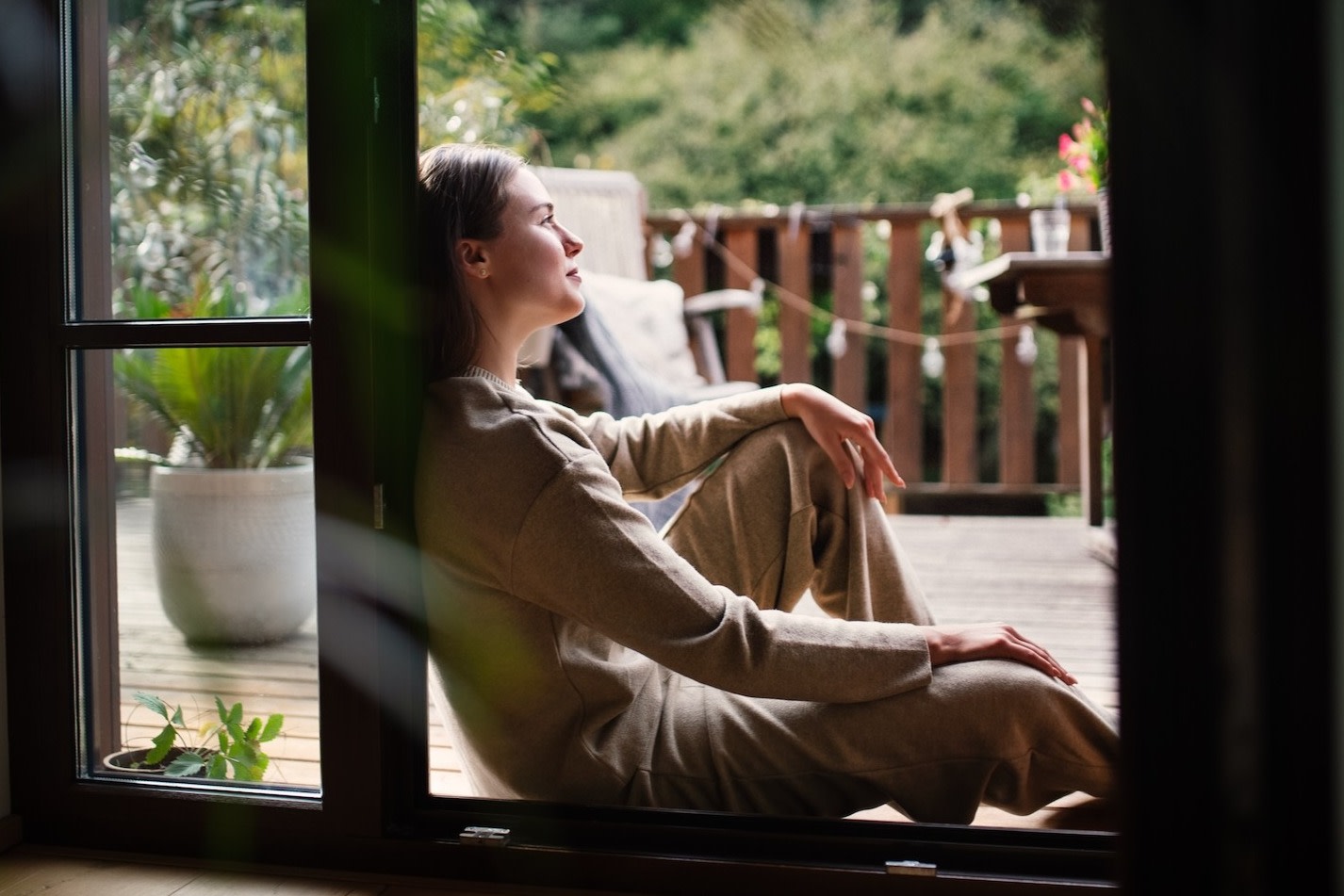 A woman sitting down at home and leaning against a doorway as she looks off into the distance outside.