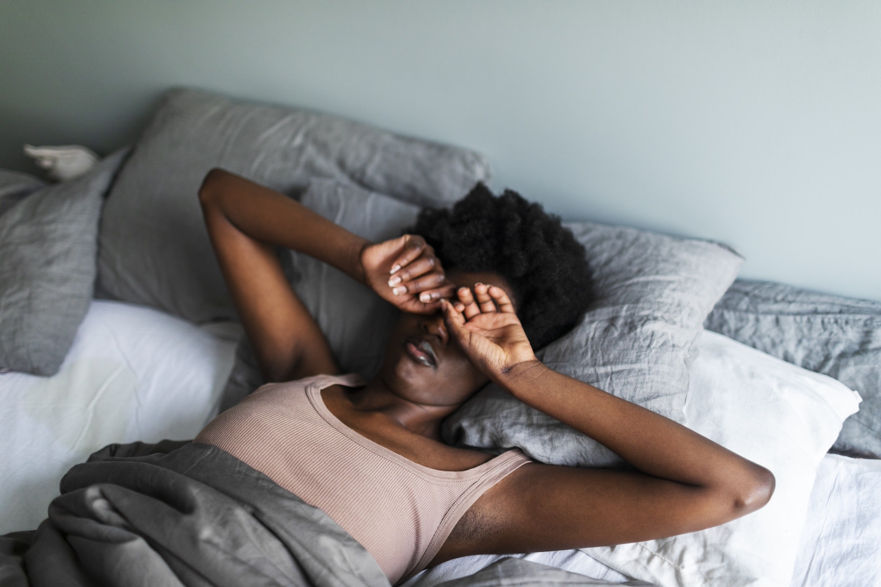 A tired woman lying in bed after getting six hours of sleep. She's rubbing her eyes.