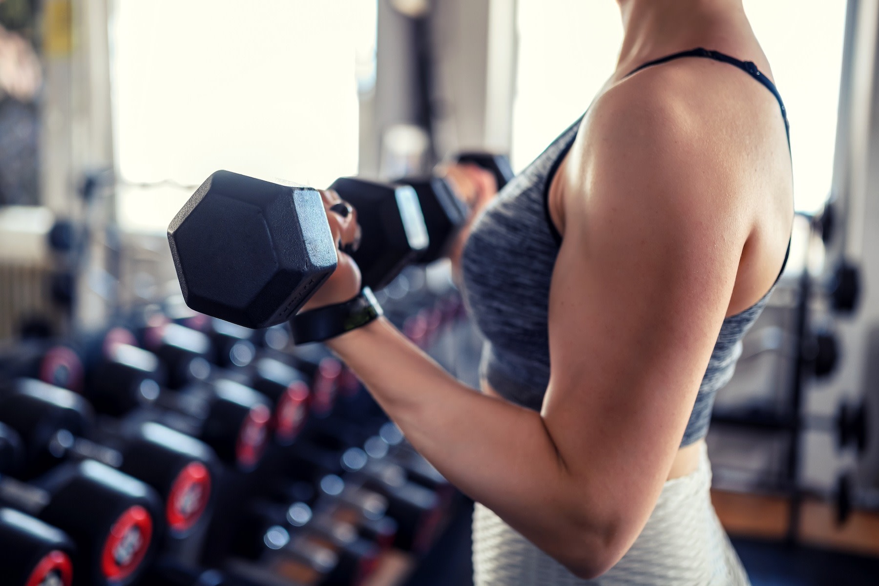 A close-up photo of a woman lifting dumbbells in a gym to build muscle.