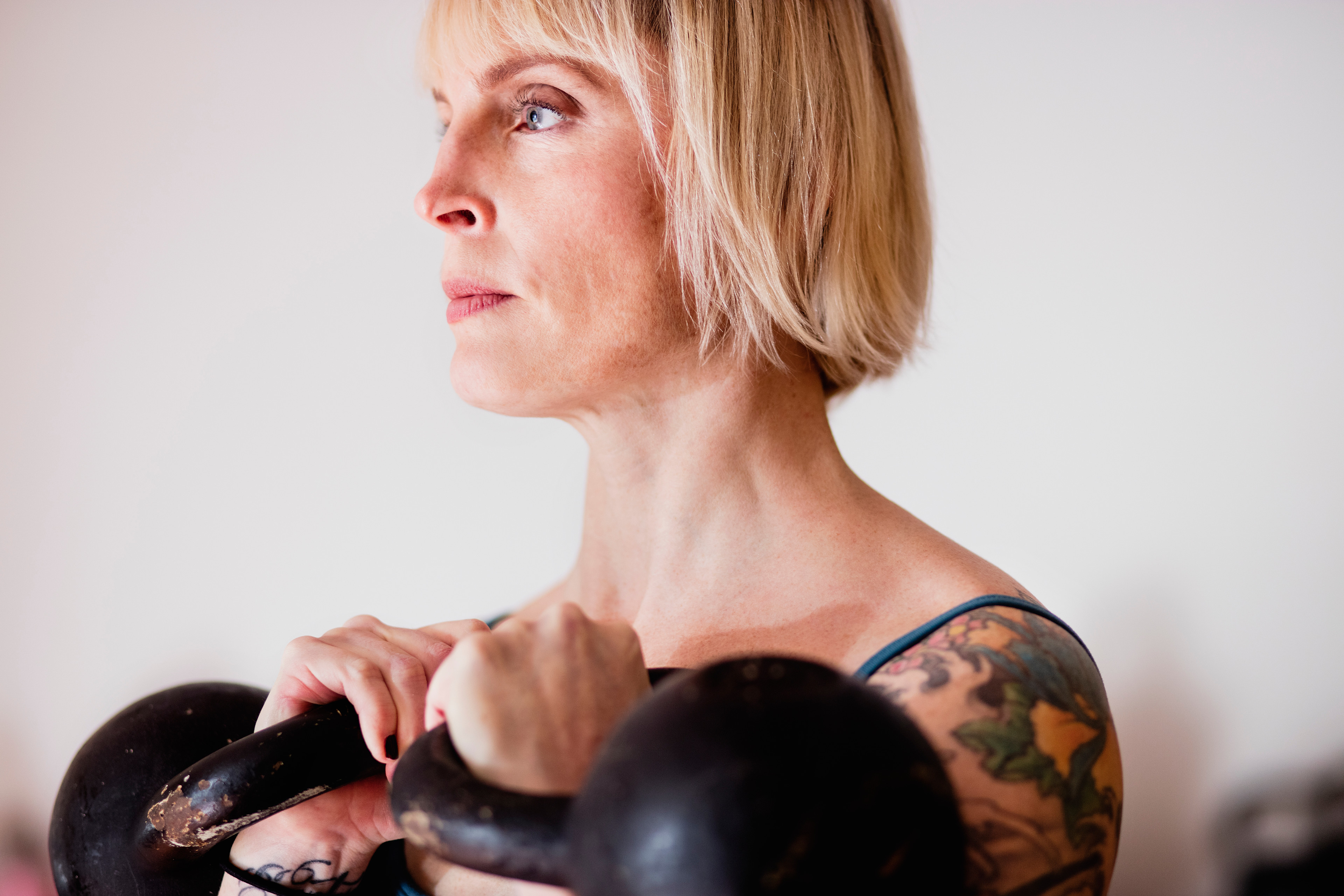 Woman with tattoos holding two kettlebells racked at shoulder height while doing kettlebell shoulder exercises