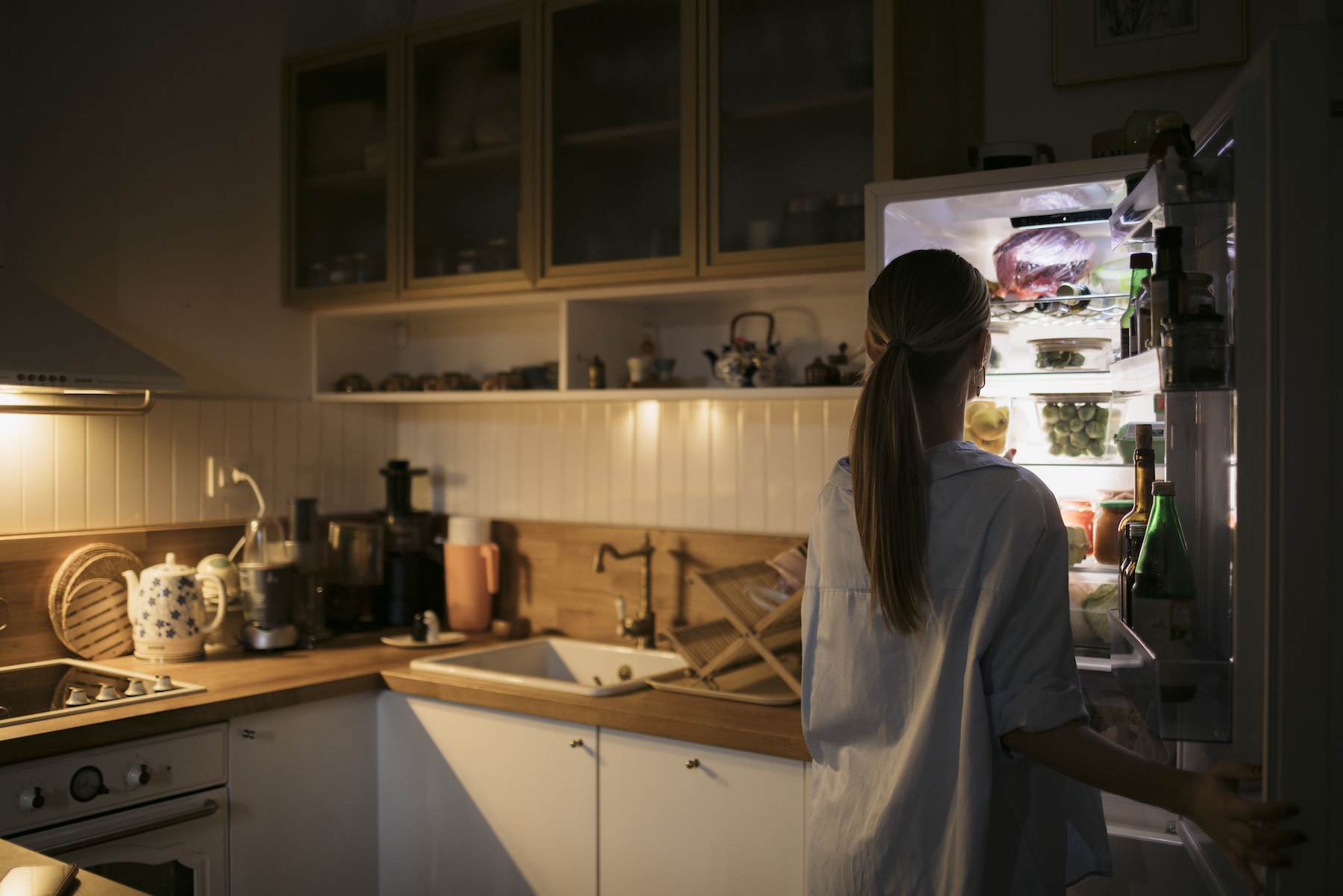 A woman standing in front of the fridge getting a bedtime snack to help her sleep.