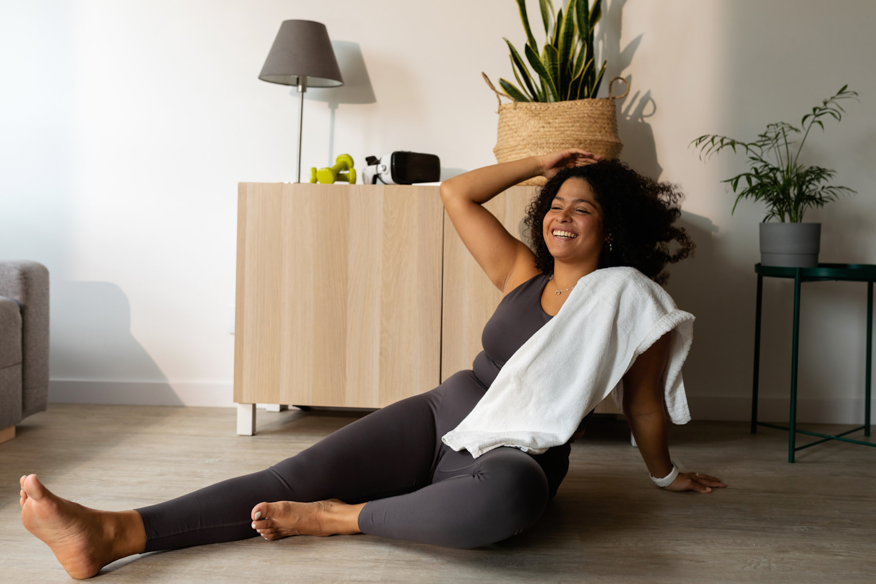 A woman smiling and sitting down on the floor after a workout. Learn how long it takes to form a habit in this article.