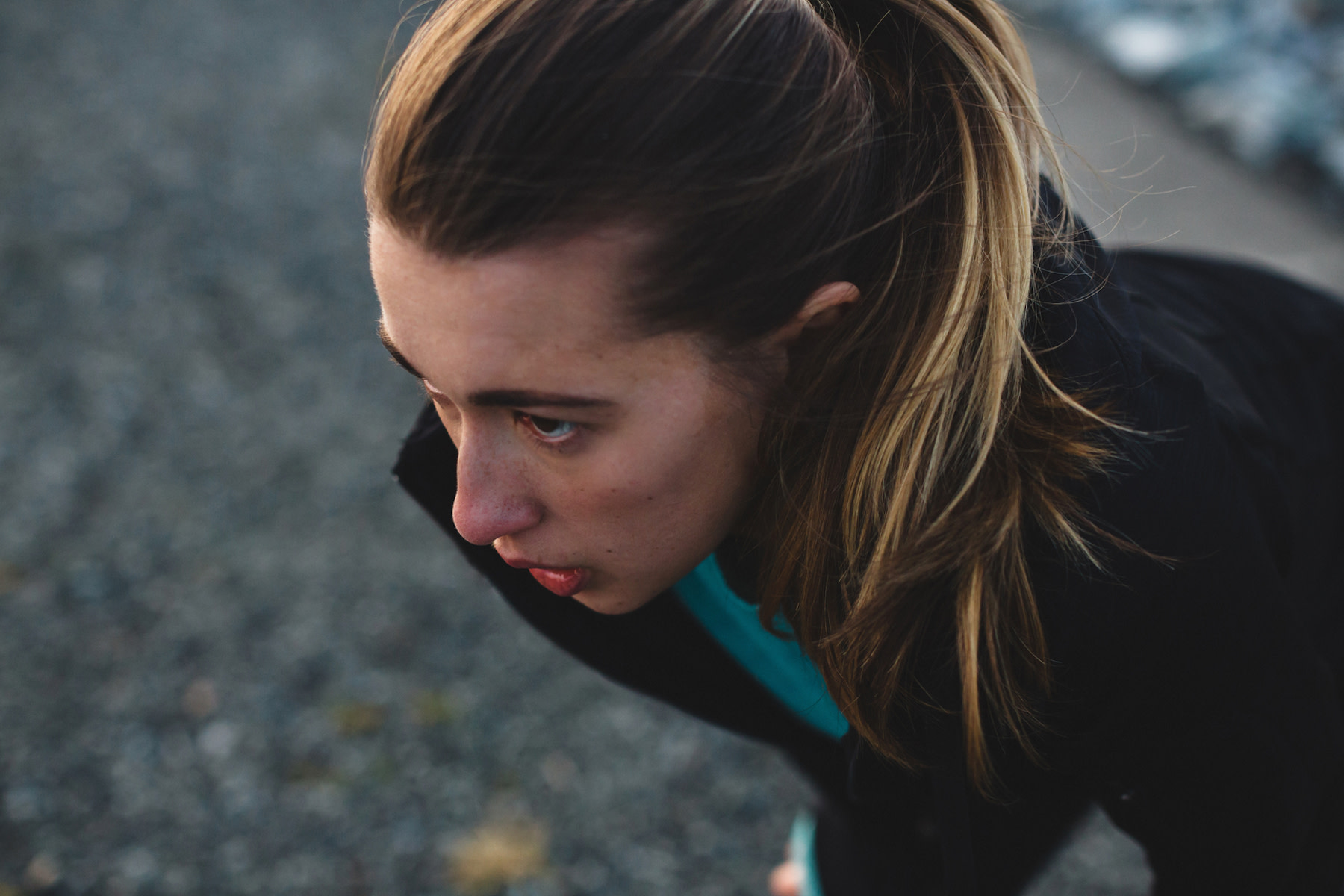 A young woman with a ponytail is bent over outside with her hands on her knees, experiencing nausea after a workout.